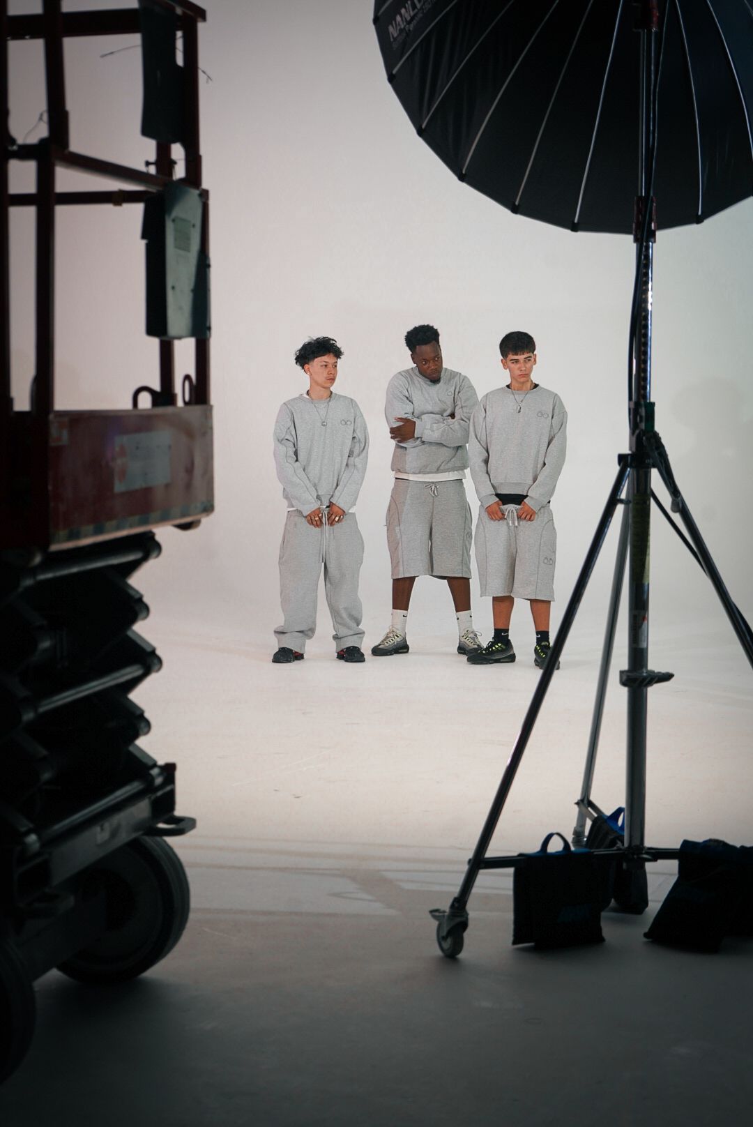 Three male models in grey matching sets stand together in a professional photography studio setup.