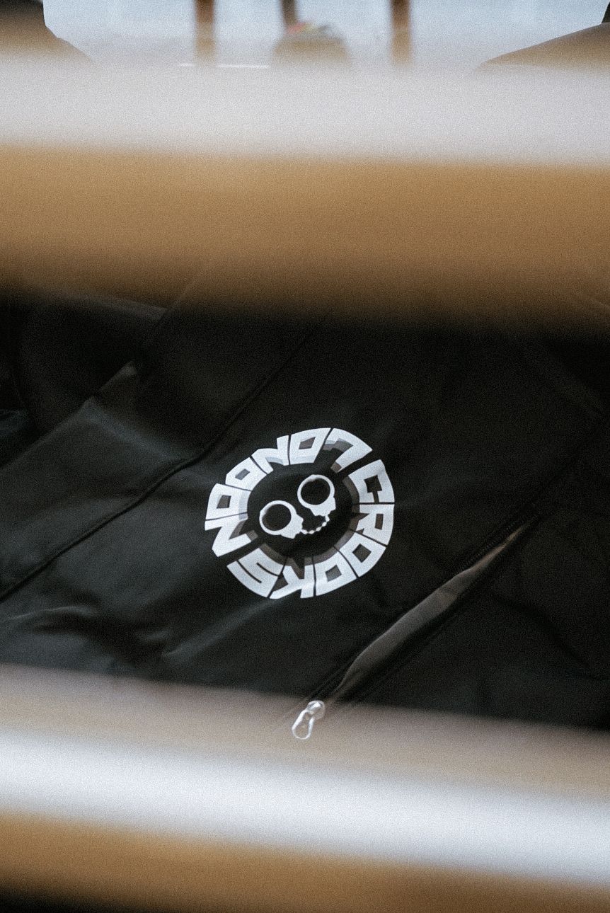 Close-up of a black Crooks and Castles logo on a dark garment viewed through a metal rack.
