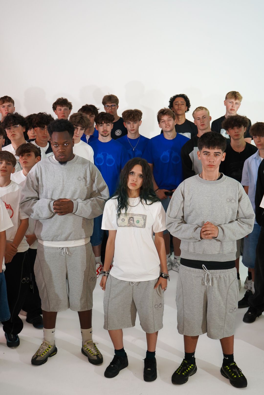 Group of young men in matching grey sweatshirts and shorts posing together in a white studio setting.