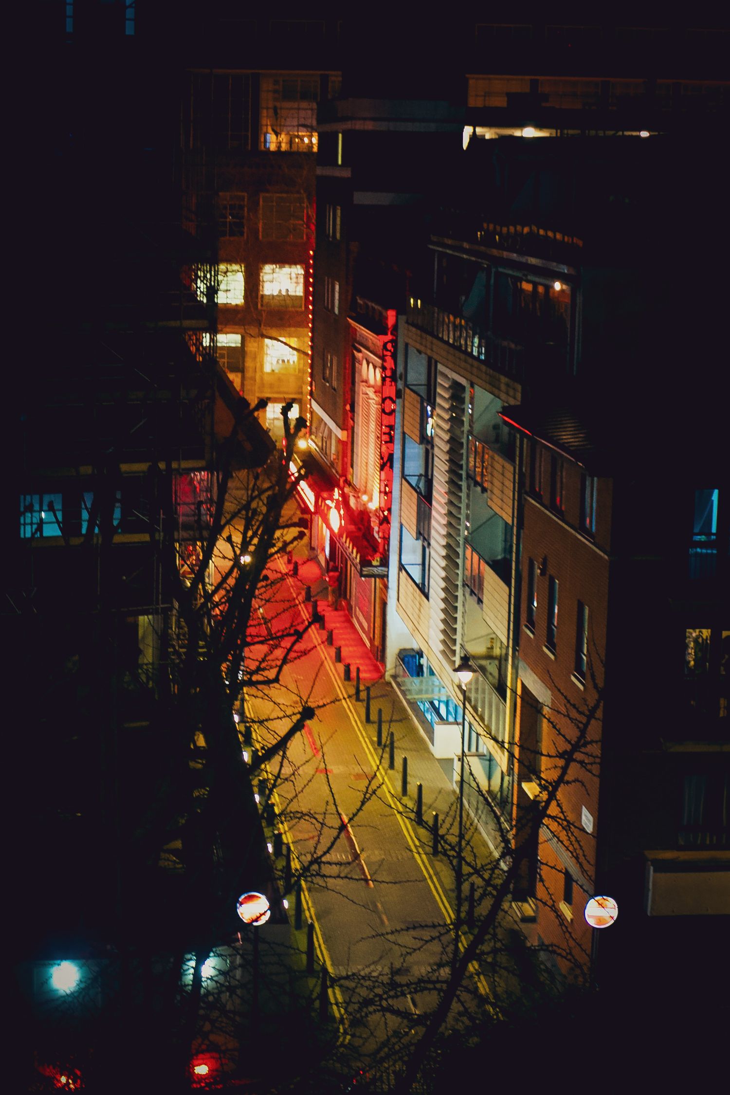 Aerial night view of a city street with glowing red and yellow lights on buildings.