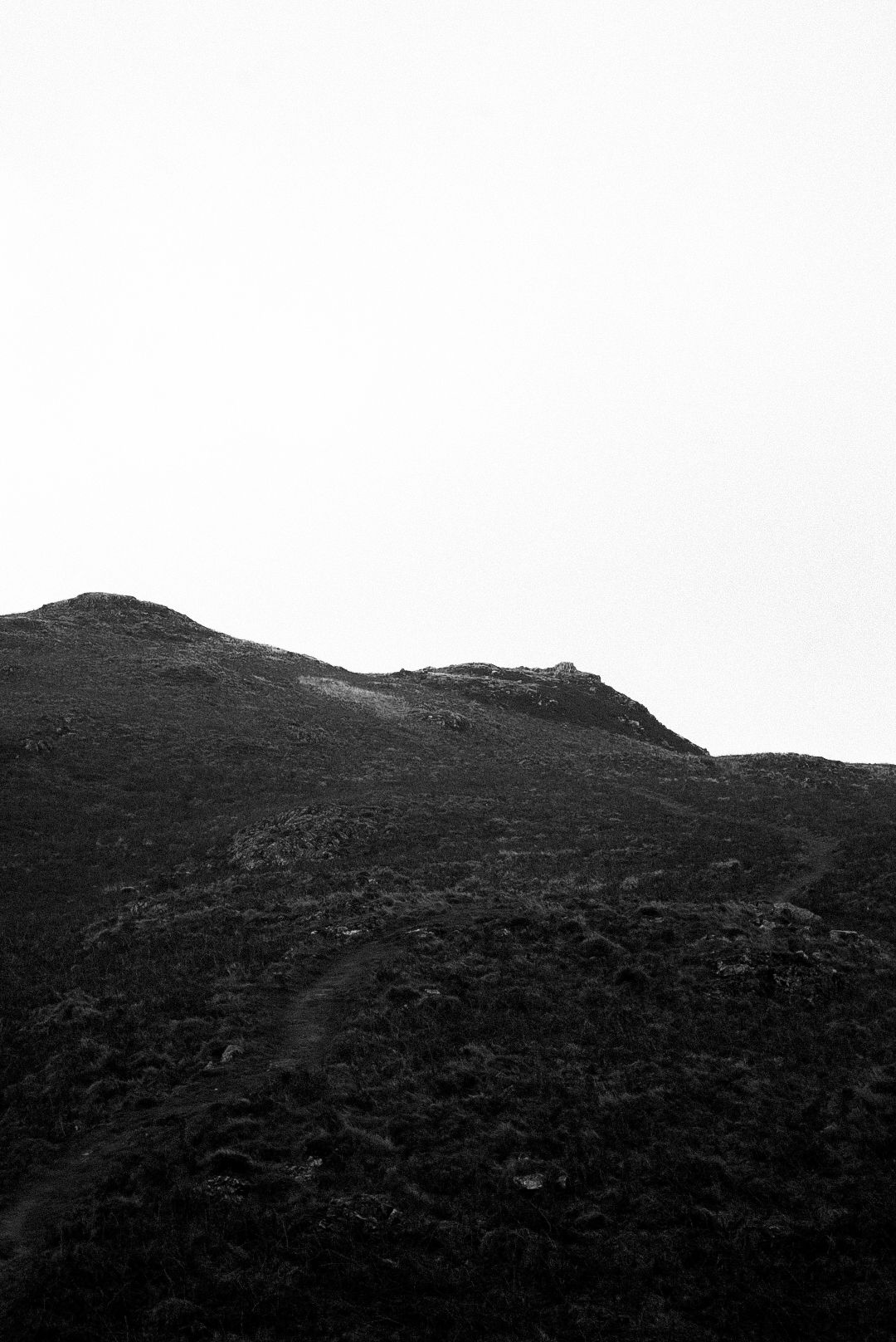 Black and white rugged mountain ridge with a narrow hiking trail on steep slope.