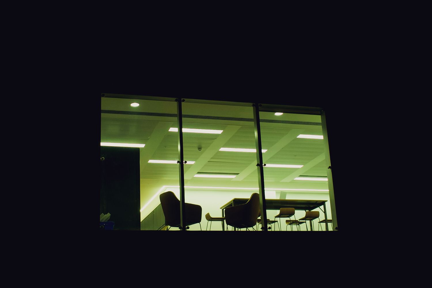Illuminated empty office conference room viewed through large glass windows at night.