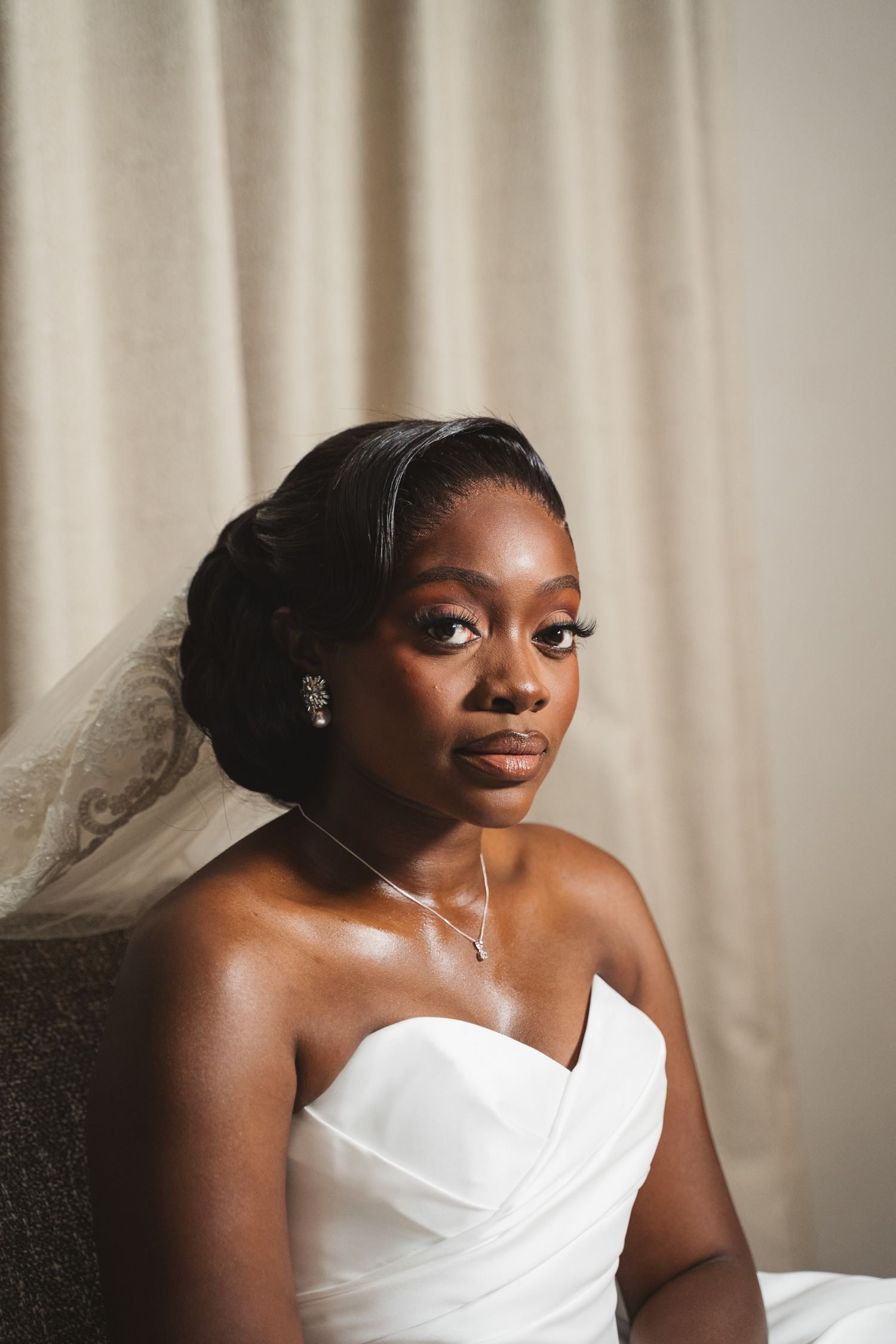 Beautiful bride in a white strapless wedding gown poses elegantly against a light curtain backdrop.