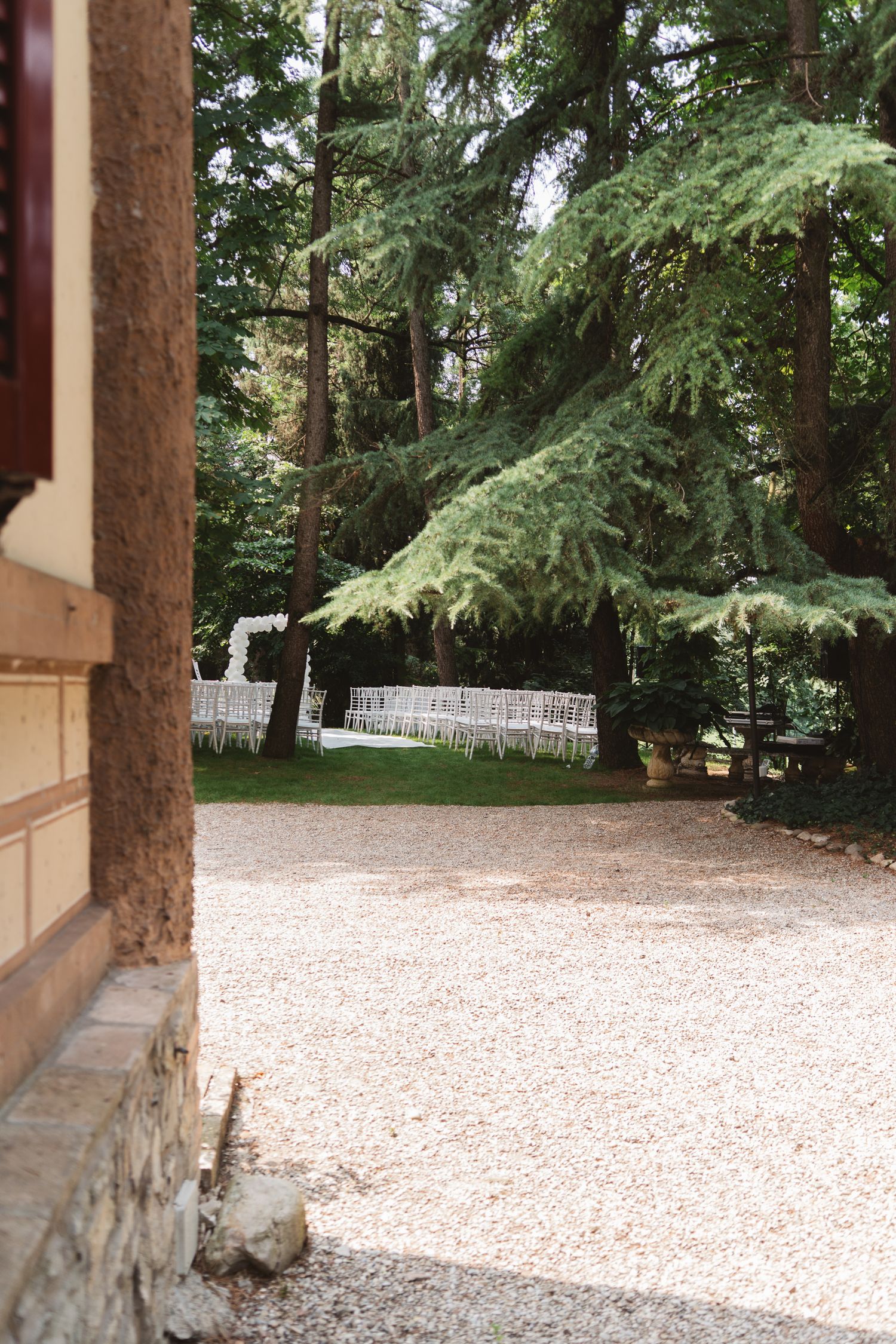 A gravel pathway winds through a tranquil garden with tall evergreen trees and white fencing.
