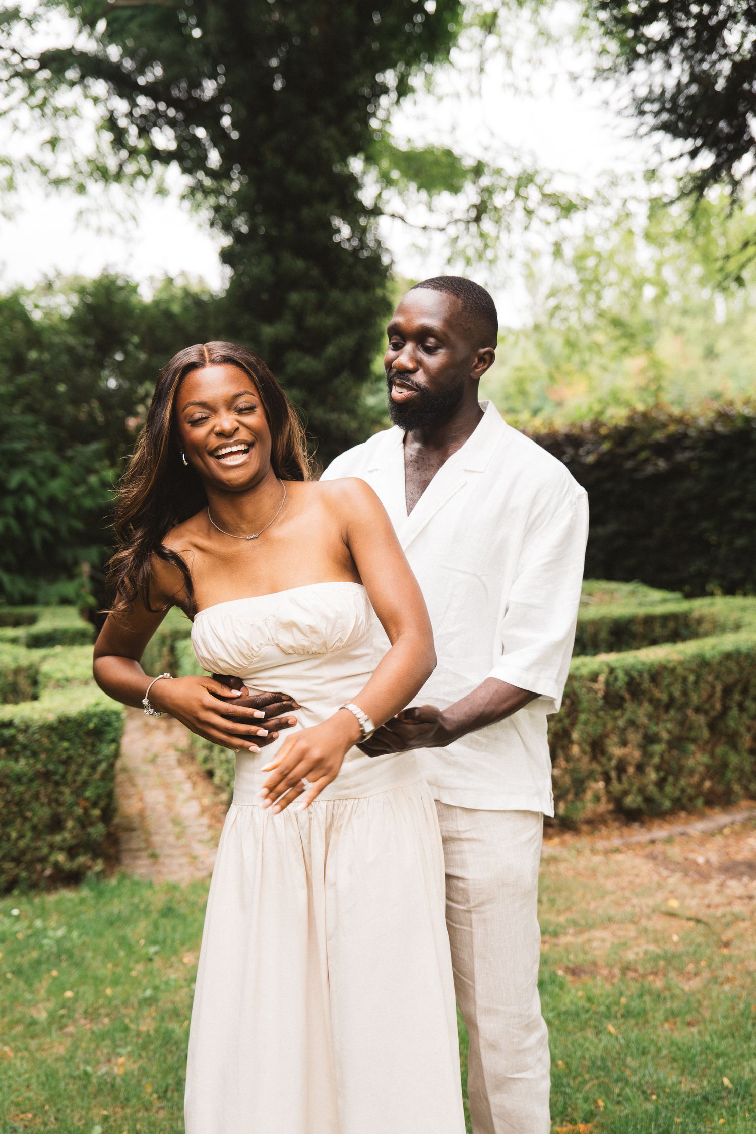 Couple in light colored outfits embracing in a garden setting.