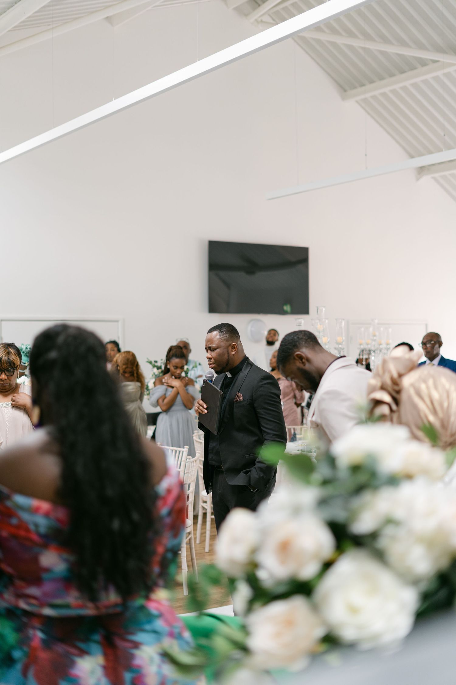 Wedding reception guests mingle in a bright indoor venue with floral decorations.