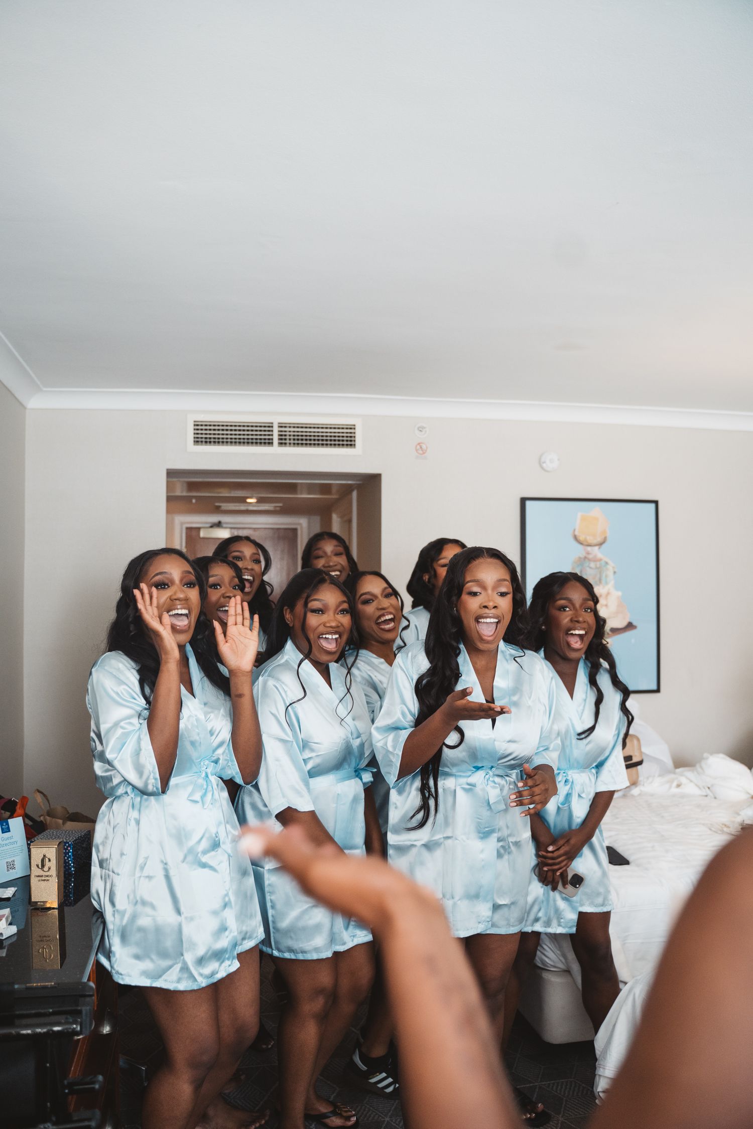 Bridesmaids in matching light blue satin robes pose together during wedding preparations.