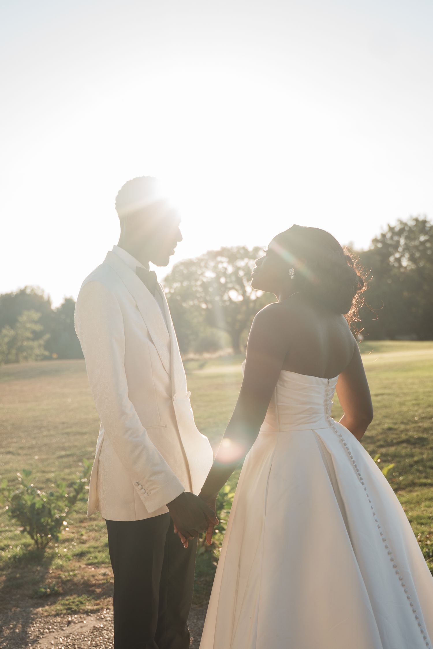 A couple in wedding attire poses together during golden hour in a field.