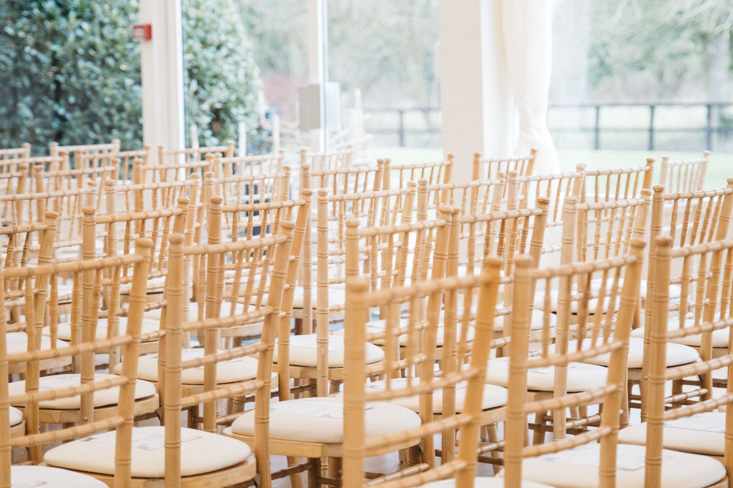 Rows of empty wooden Chiavari chairs set up for an elegant indoor wedding ceremony.