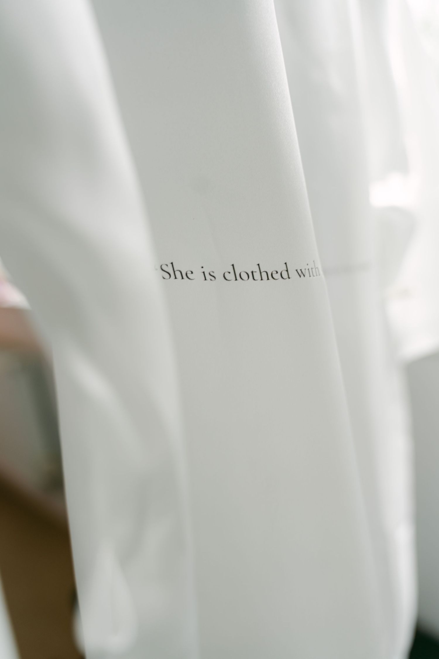 Close-up of white fabric with text 'She is clothed with'.