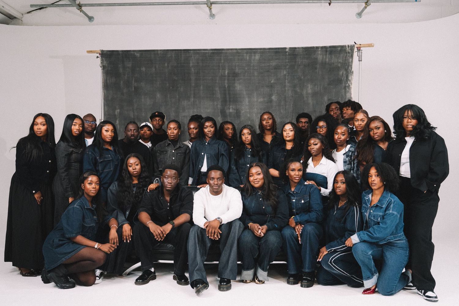 Large group portrait of people wearing dark clothing seated and standing against a white background.