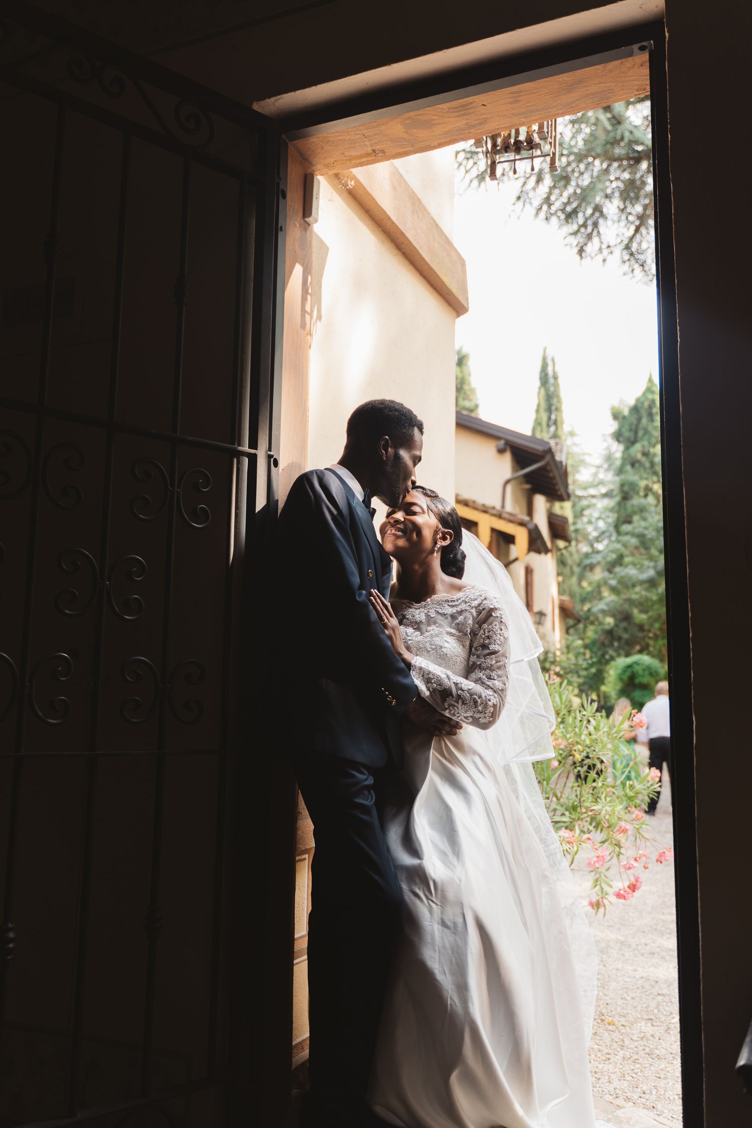 A romantic silhouette of a couple framed in a doorway against a sunlit garden.