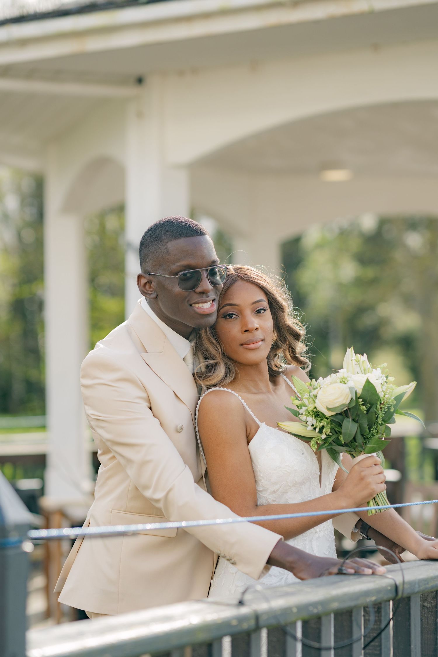 Newlyweds share intimate moment on gazebo deck with white floral bouquet.