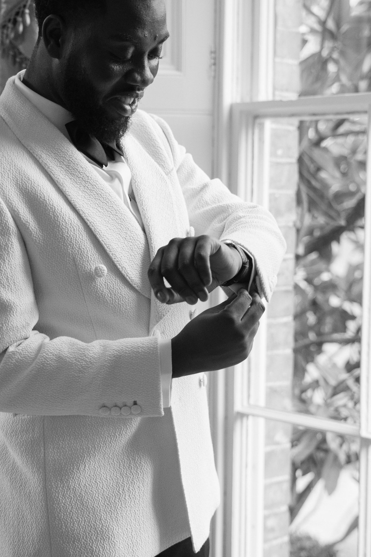 Black and white photo of someone adjusting cufflinks by a window.