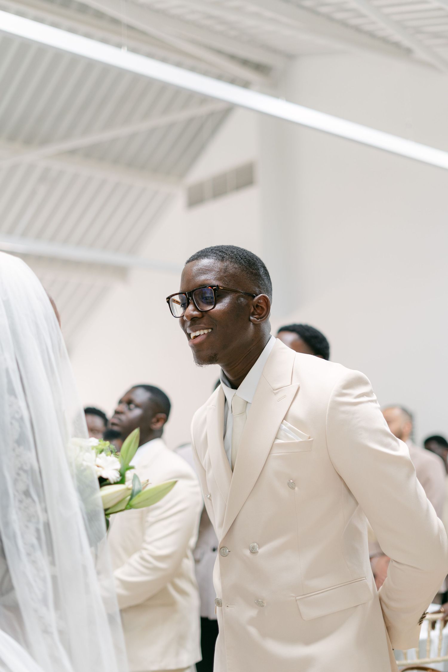 Joyful wedding party members in cream-colored suits celebrate during an indoor reception.
