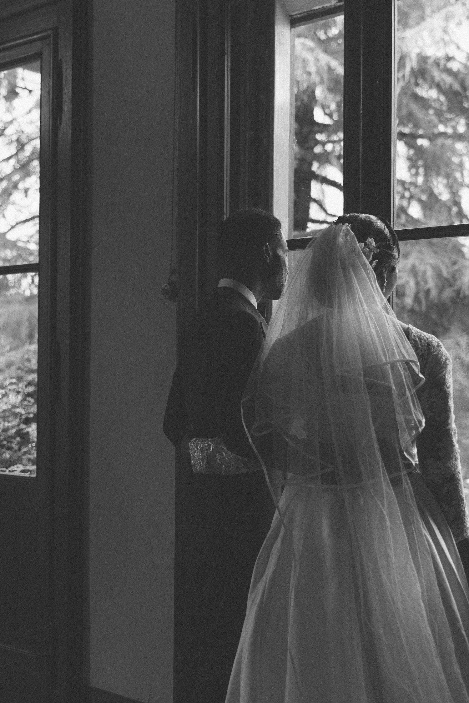 Silhouettes of wedding party against bright windows in moody lighting.
