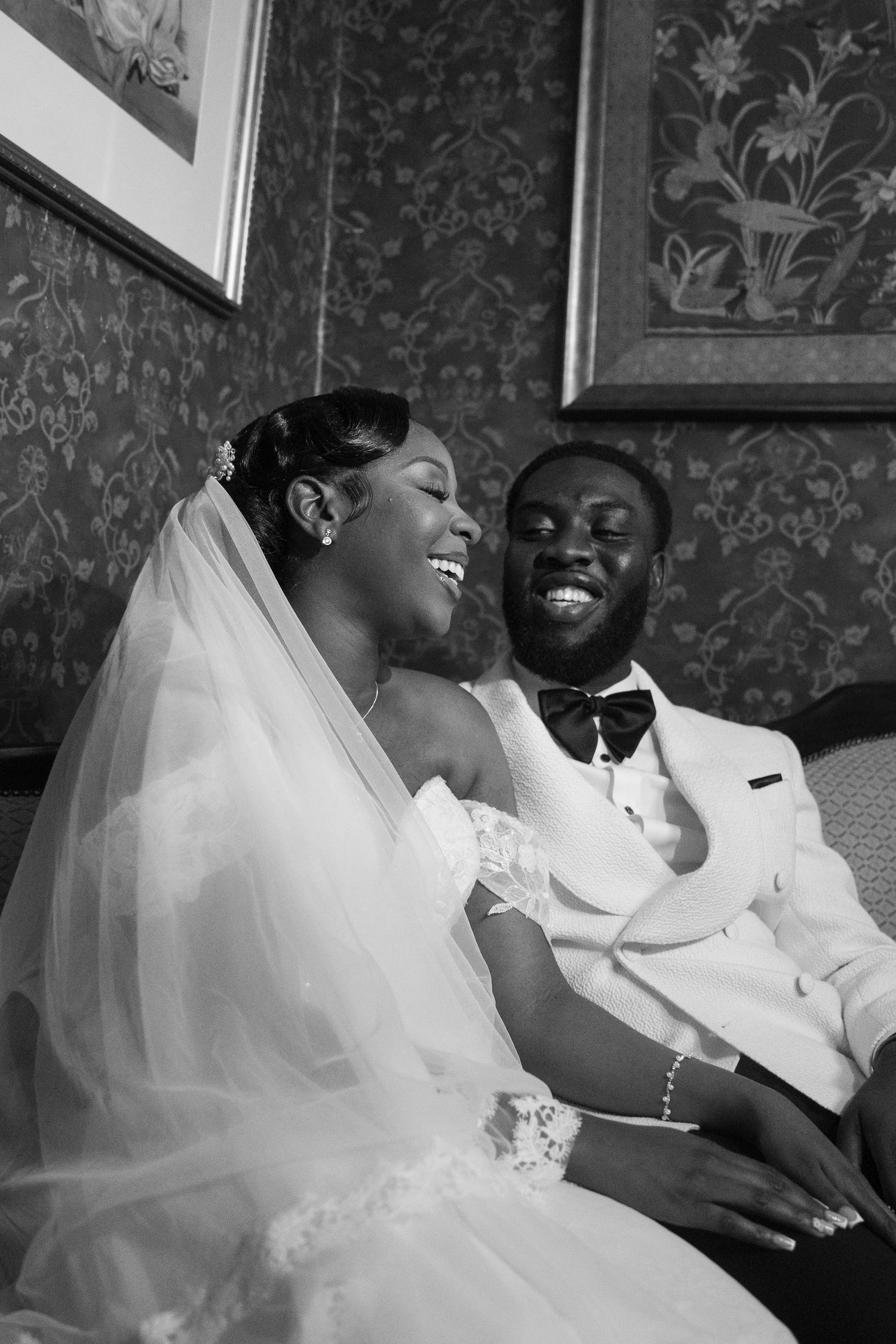 A couple laughs together while sitting on a couch in a vintage-styled room.