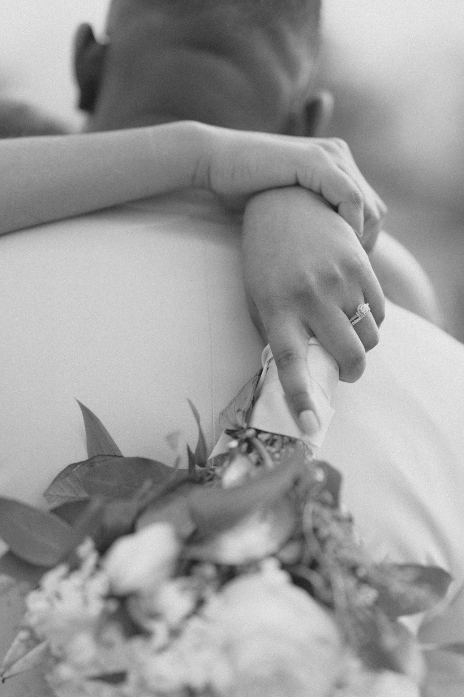 Black and white detail shot of hands holding a wedding bouquet.