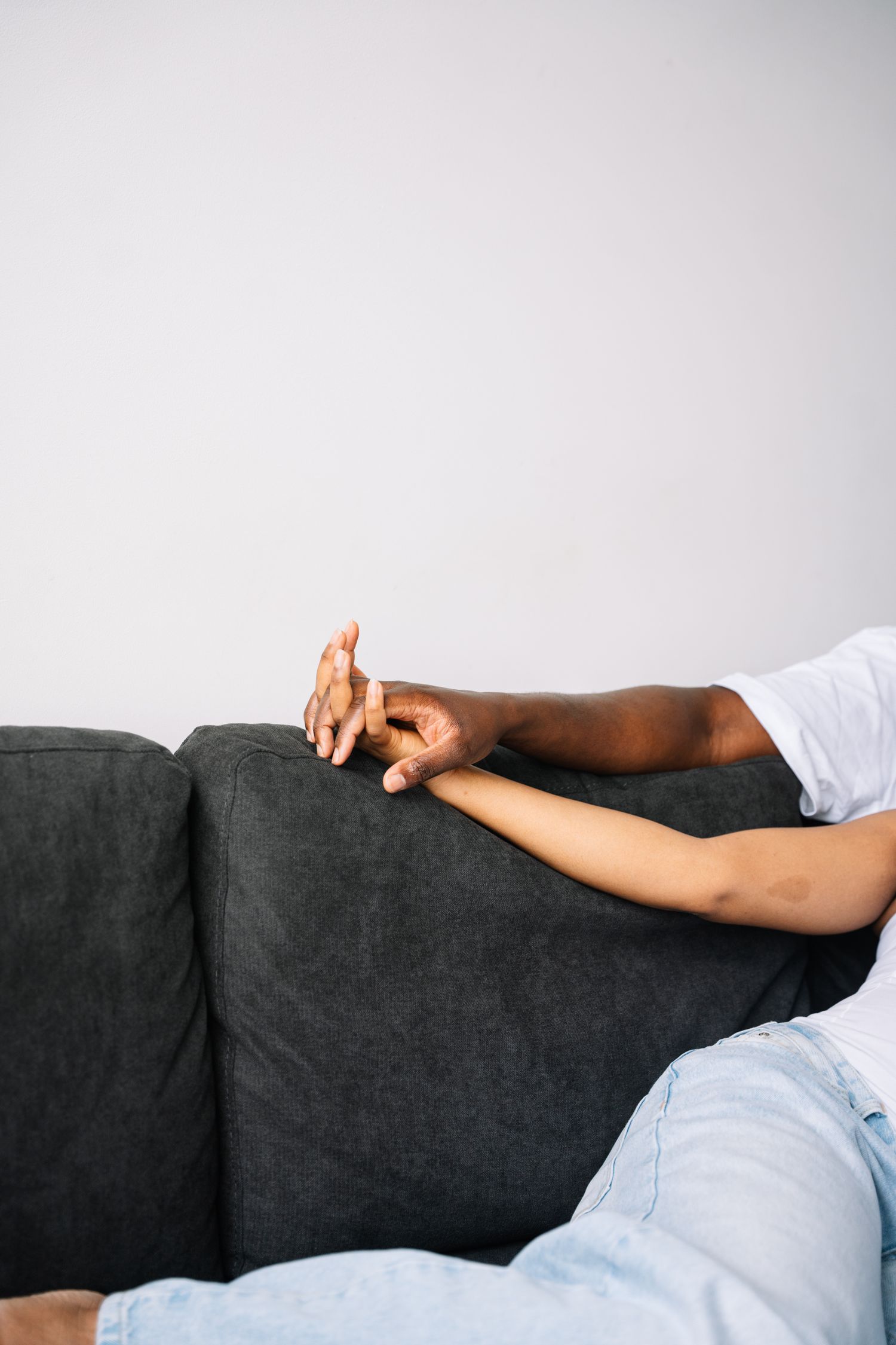 Person relaxing on dark gray couch shown from side angle against white background.