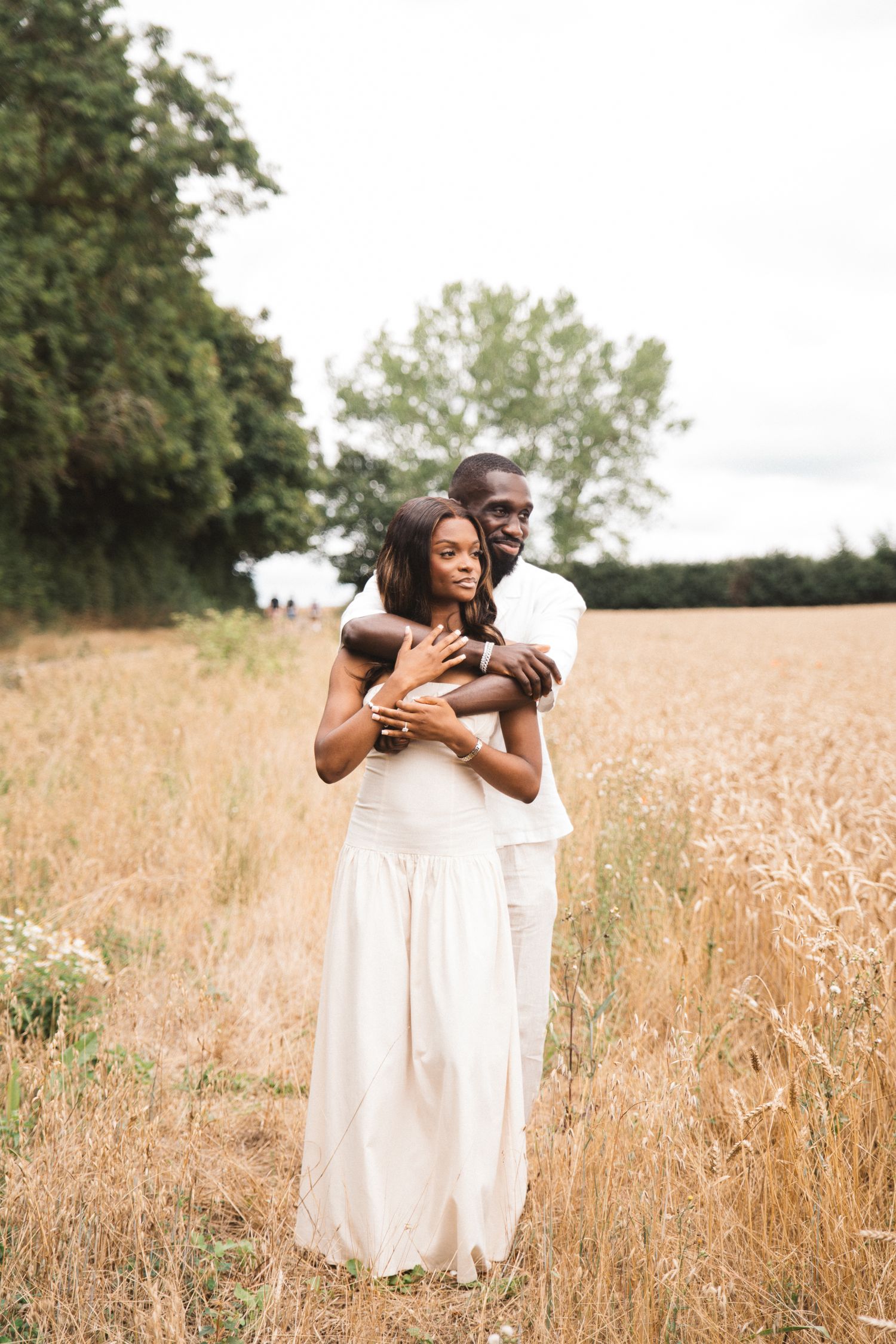 Two people in white dresses embrace in a golden wheat field on a sunny day.