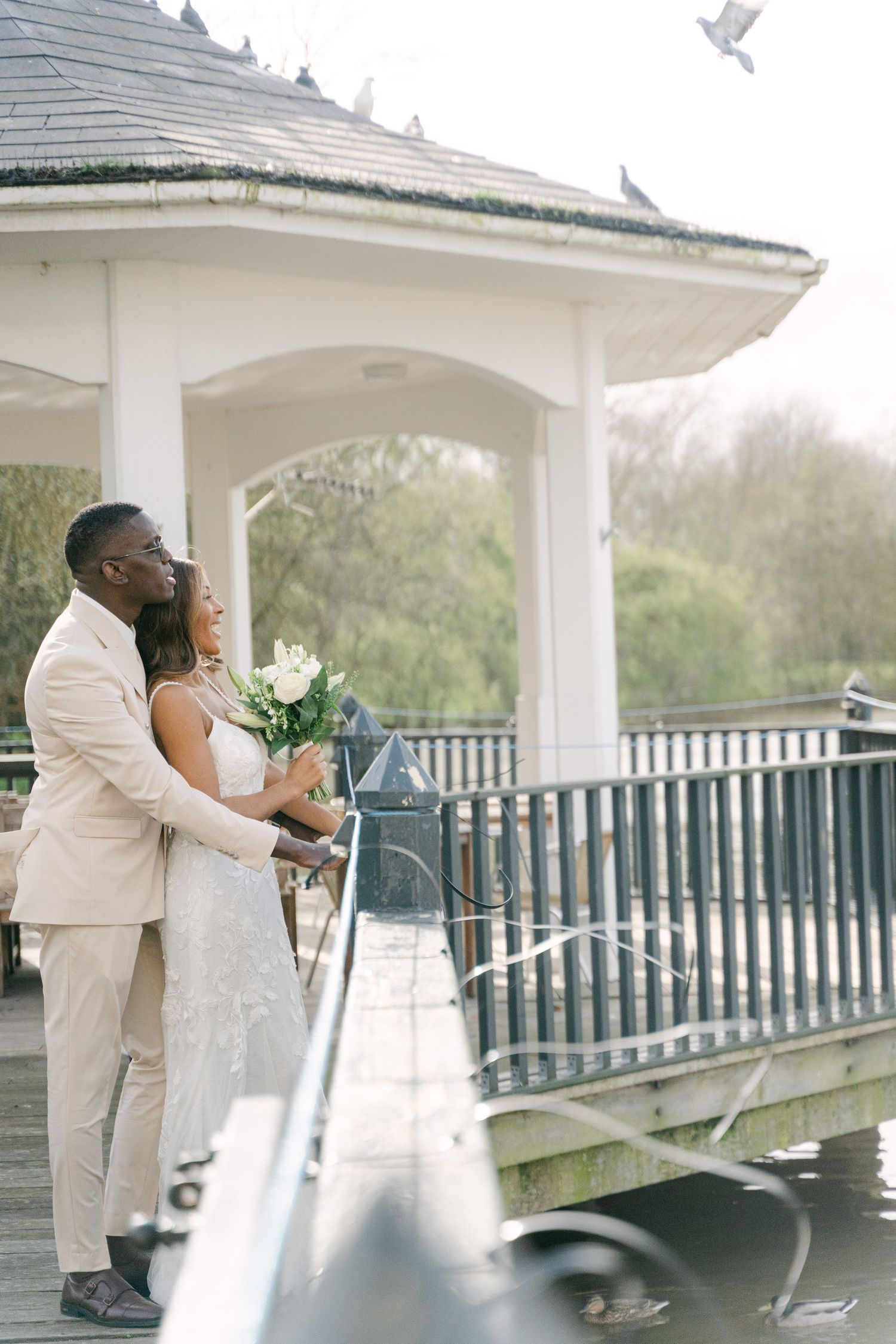 Romantic wedding couple poses on white gazebo deck with doves flying overhead.
