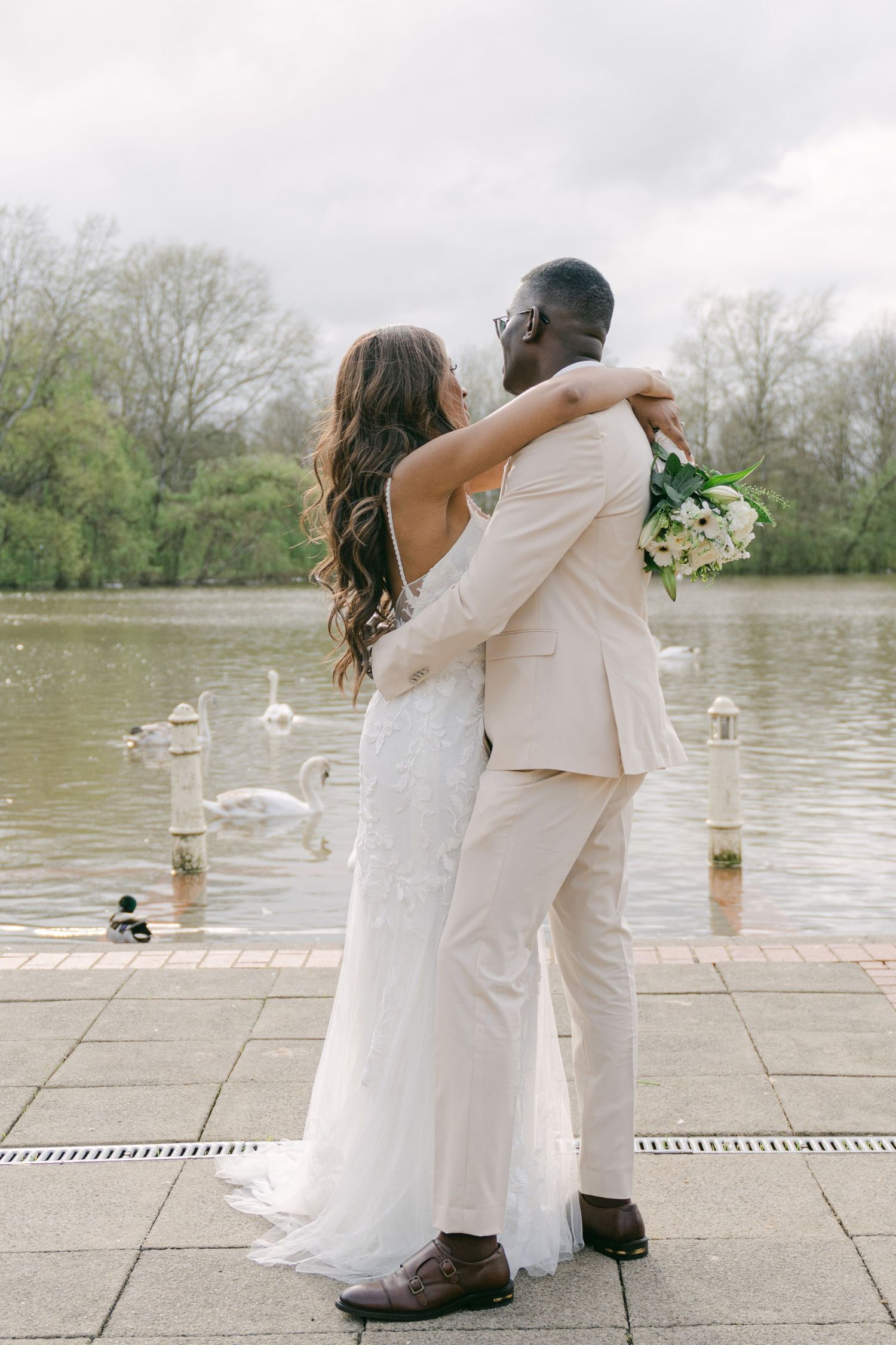 Wedding couple shares an intimate moment by a lakeside with swans in the background.
