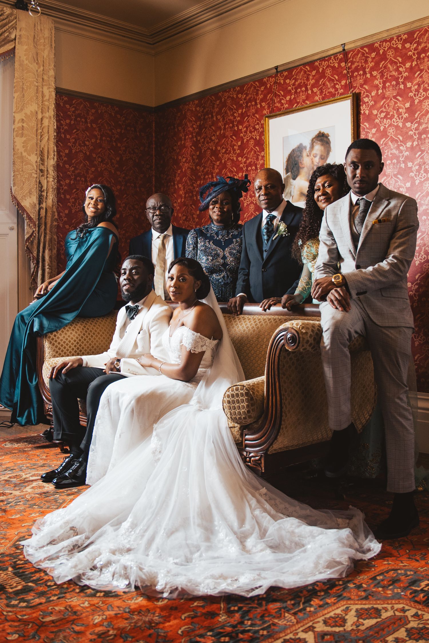 Bride in flowing white gown sits on vintage couch with wedding party members.