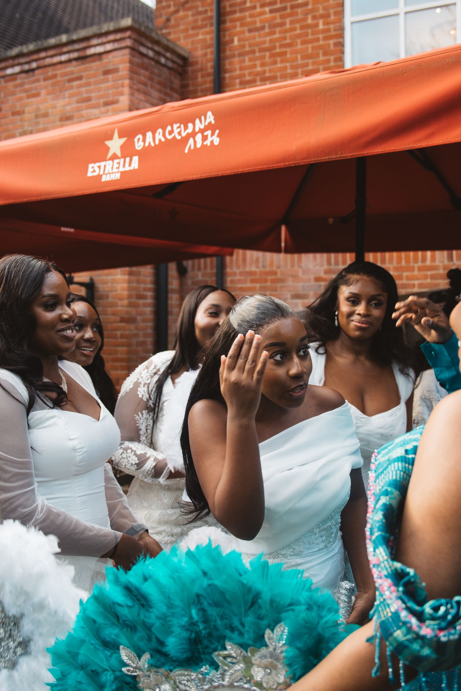 Bridesmaids in white and turquoise outfits gather outside brick building.