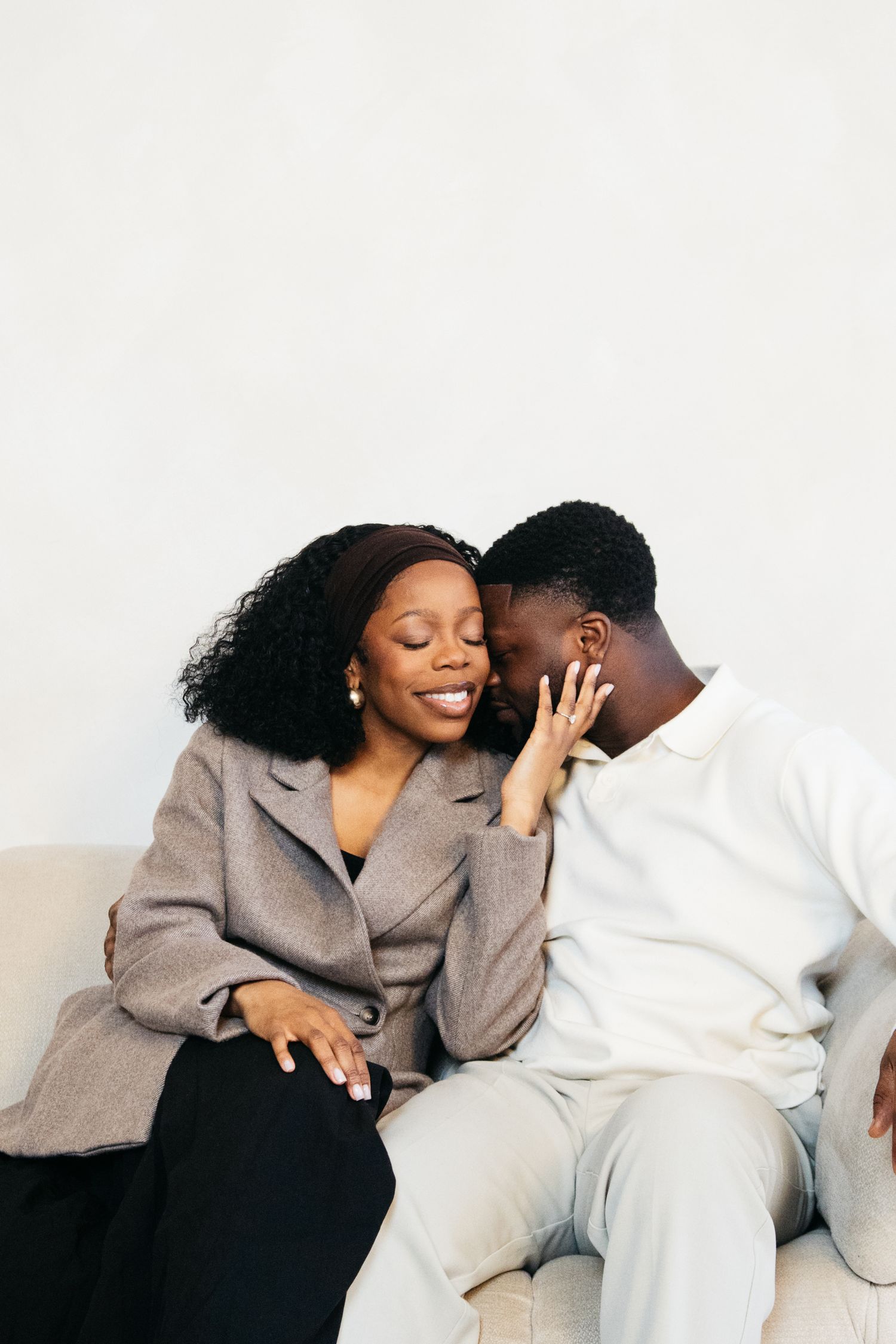 A loving Black couple sitting close together on a sofa, sharing an intimate moment, smiling and whispering.