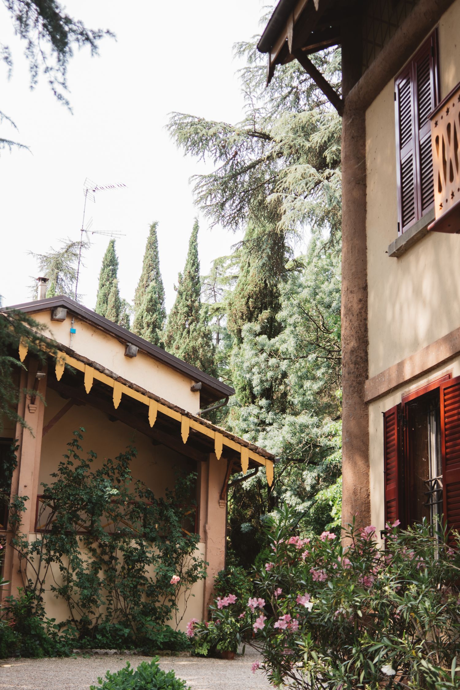 Mediterranean-style villa with cypress trees and pink flowers blooming along the facade.