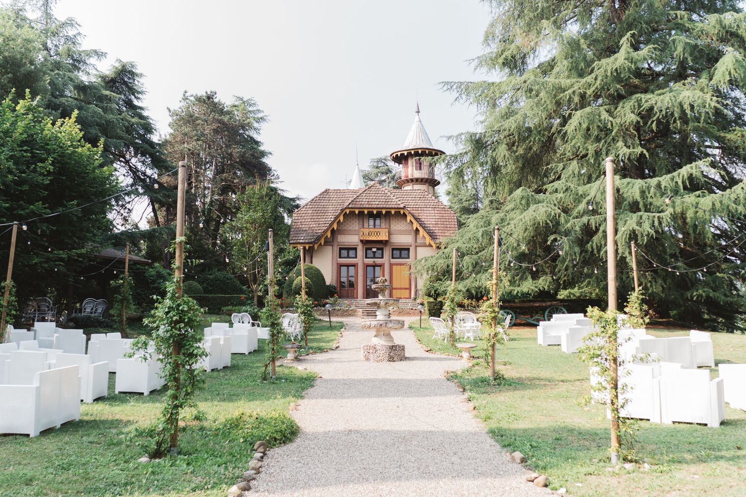 A rustic wedding venue with white chairs set up along a path leading to a charming building.