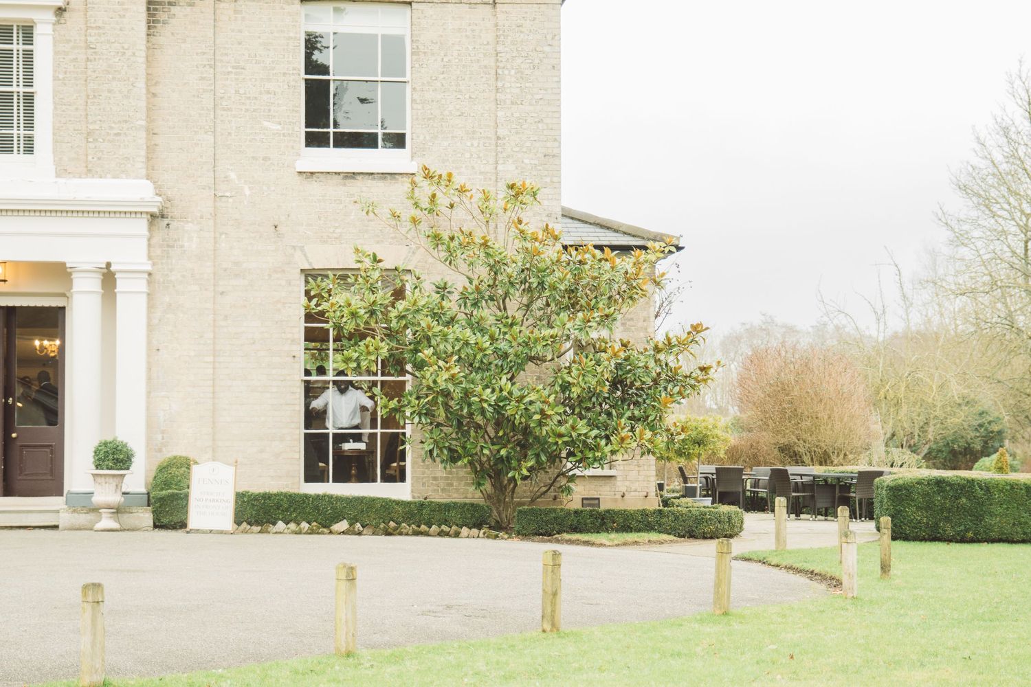 Front view of a classic white manor house with manicured lawn and wooden post barriers.