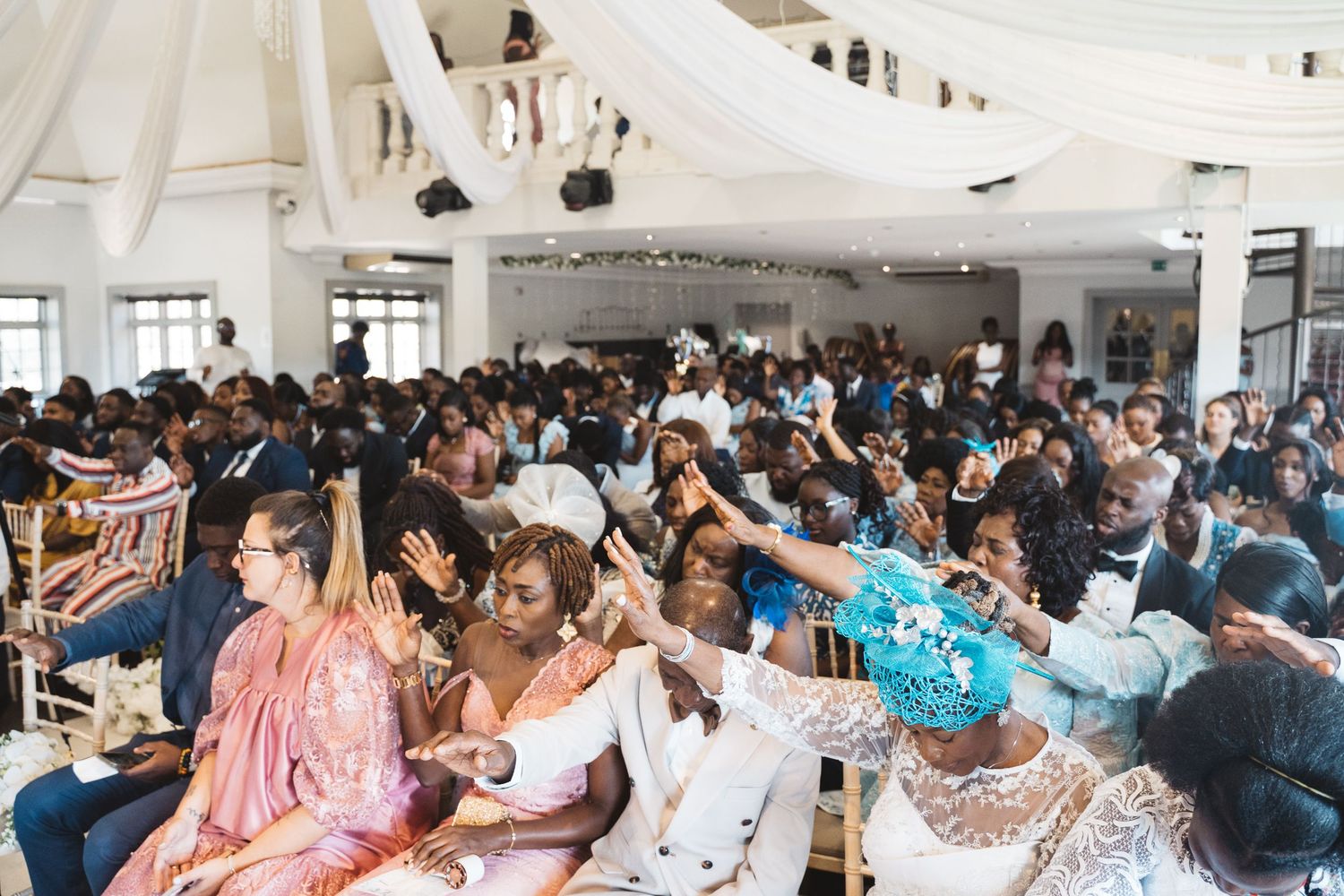 Excited wedding guests celebrating with raised hands in a bright venue filled with people.