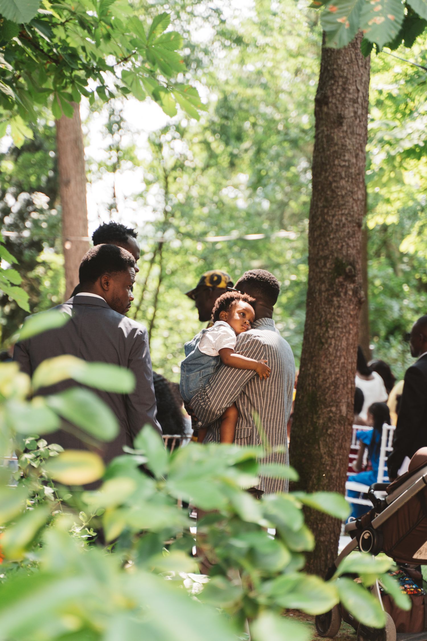 A tender moment captured through foliage at an outdoor wedding gathering.