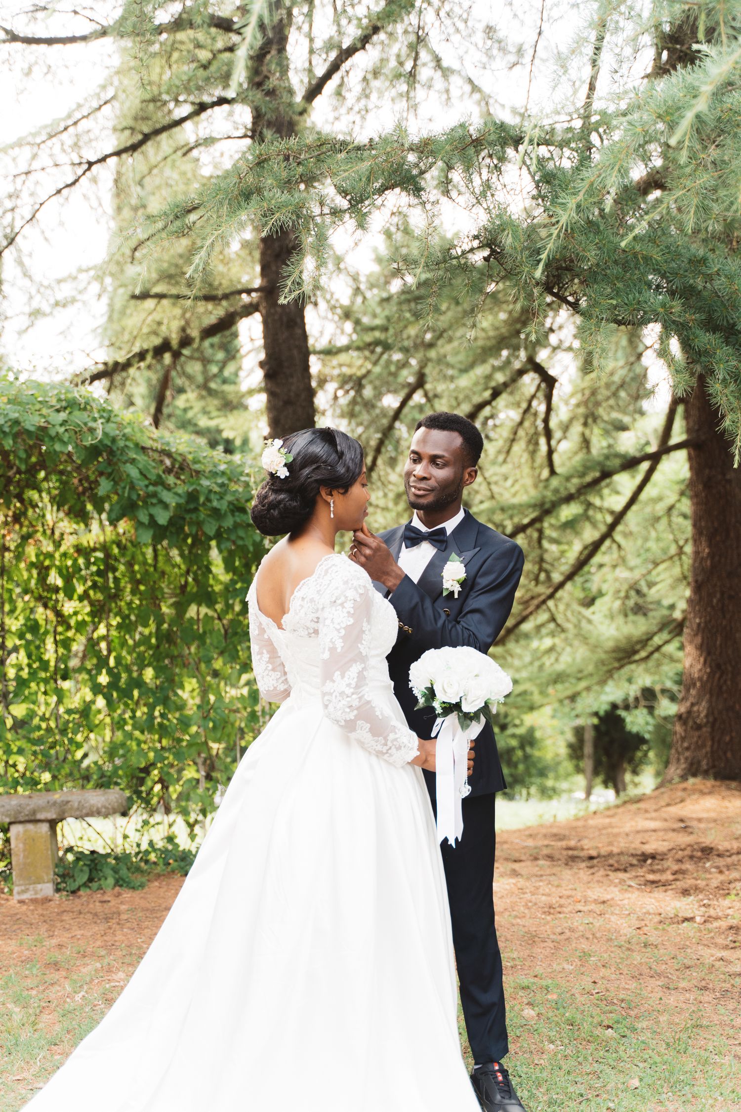Wedding couple sharing a romantic moment under tall evergreen trees.