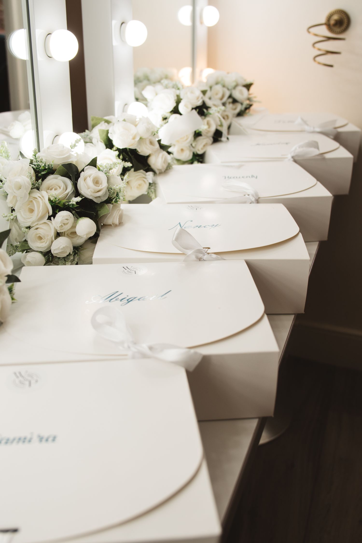 Elegant white wedding favors and gift boxes arranged in a row with white rose floral decorations.