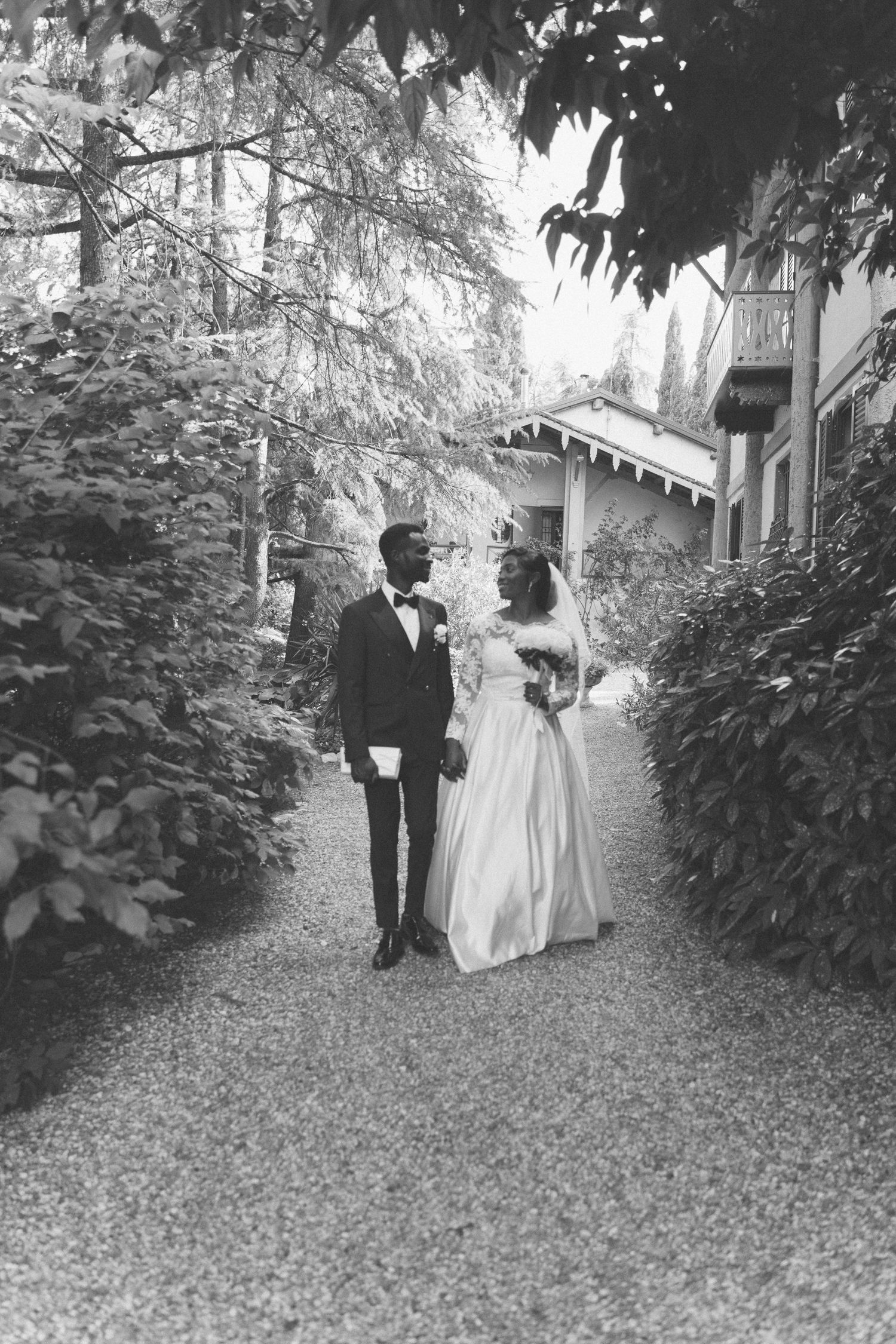 Wedding couple walking through a garden path surrounded by lush greenery in black and white.