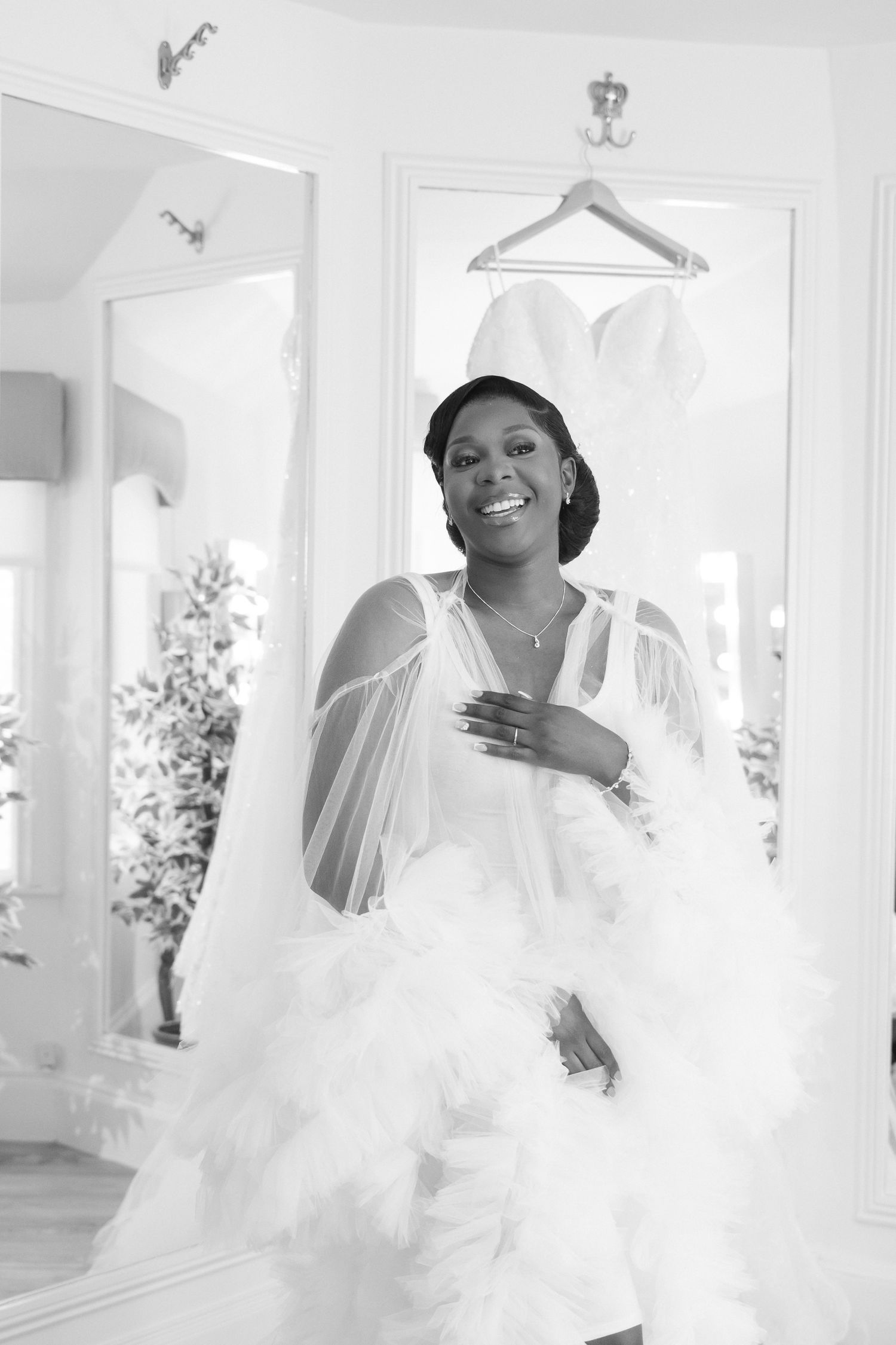 Black and white portrait showing a wedding dress preparation scene in a bright room.