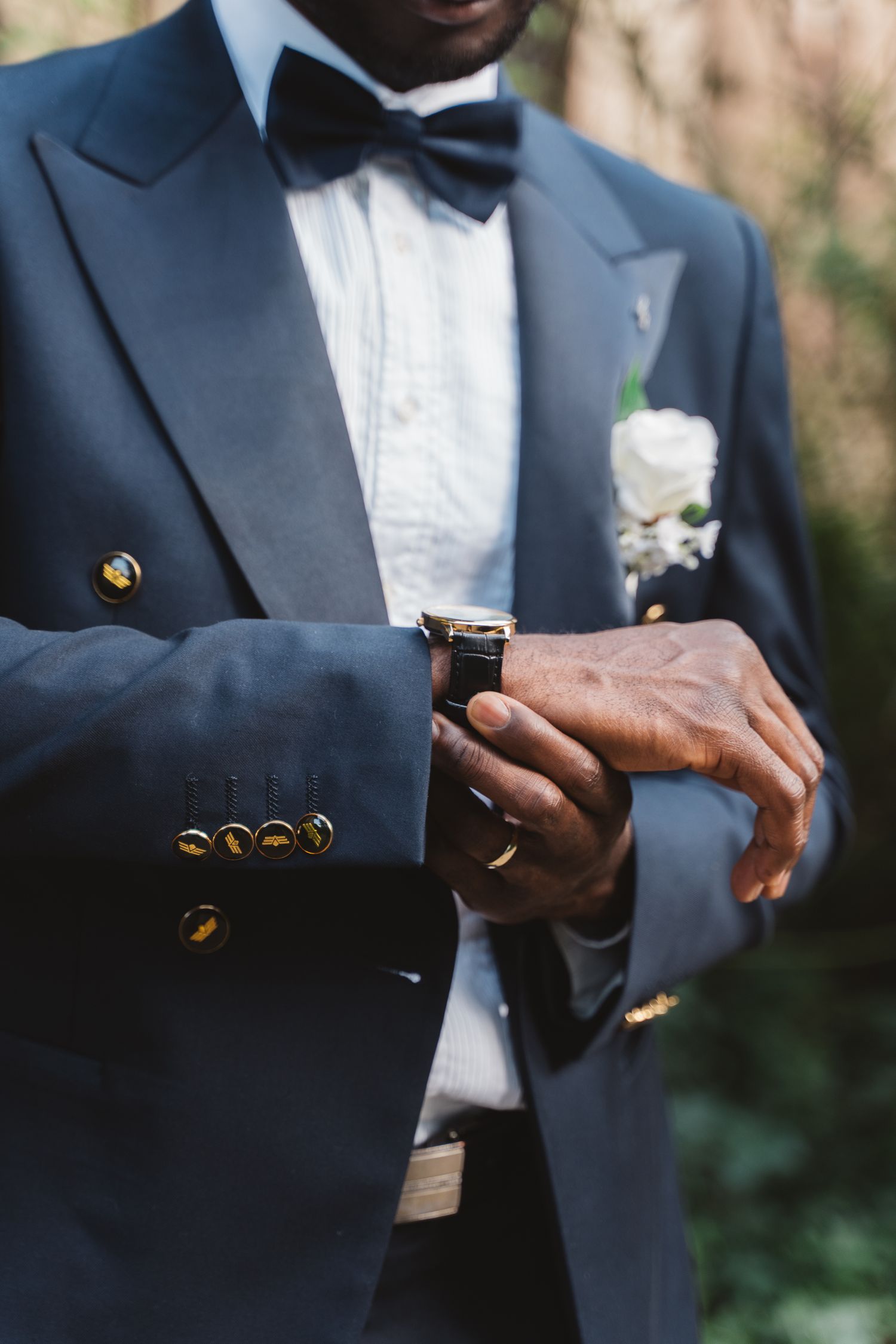 Close-up details of navy tuxedo jacket with gold buttons and white shirt.