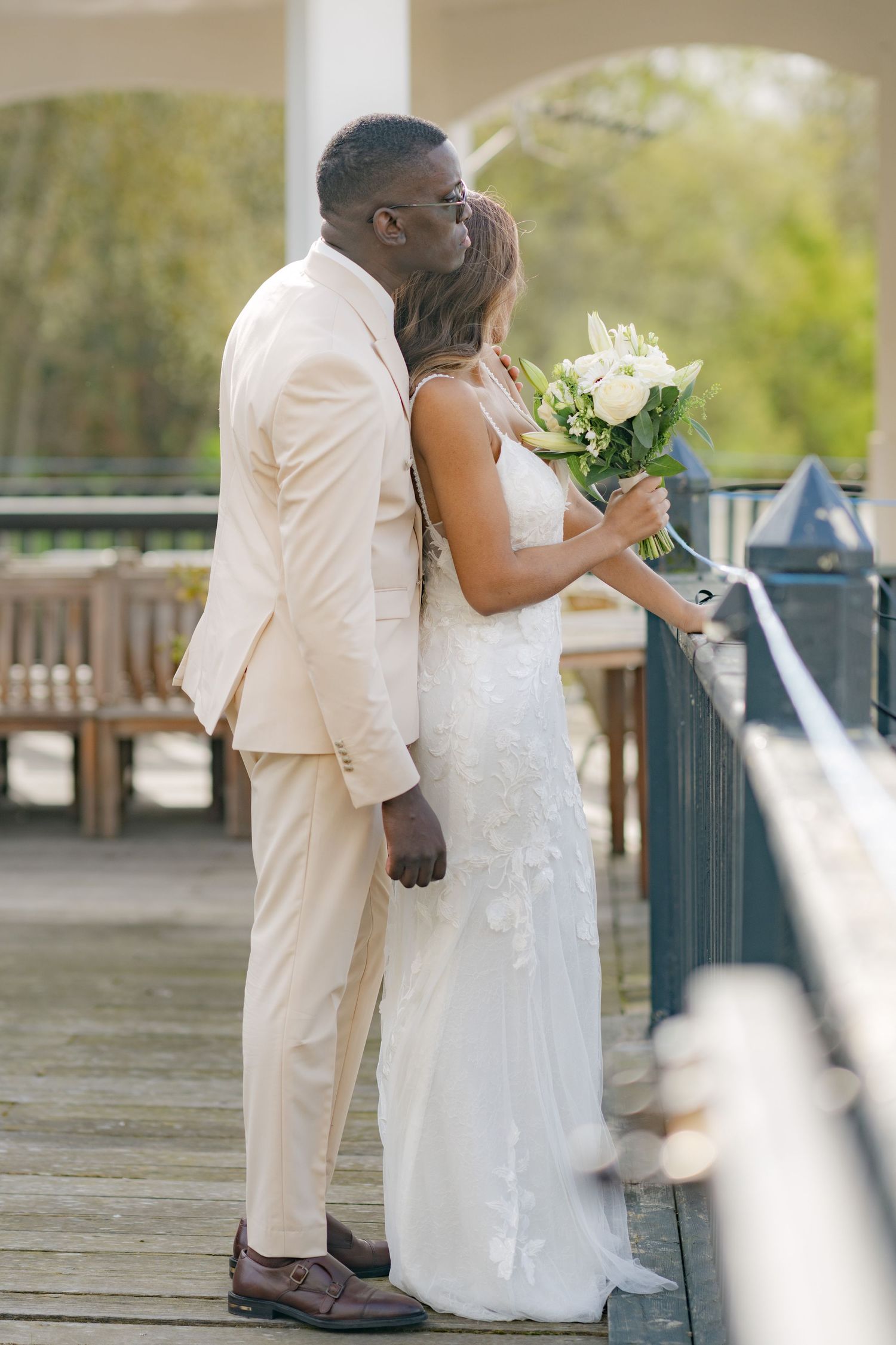 Wedding couple poses together on outdoor deck with elegant white attire.