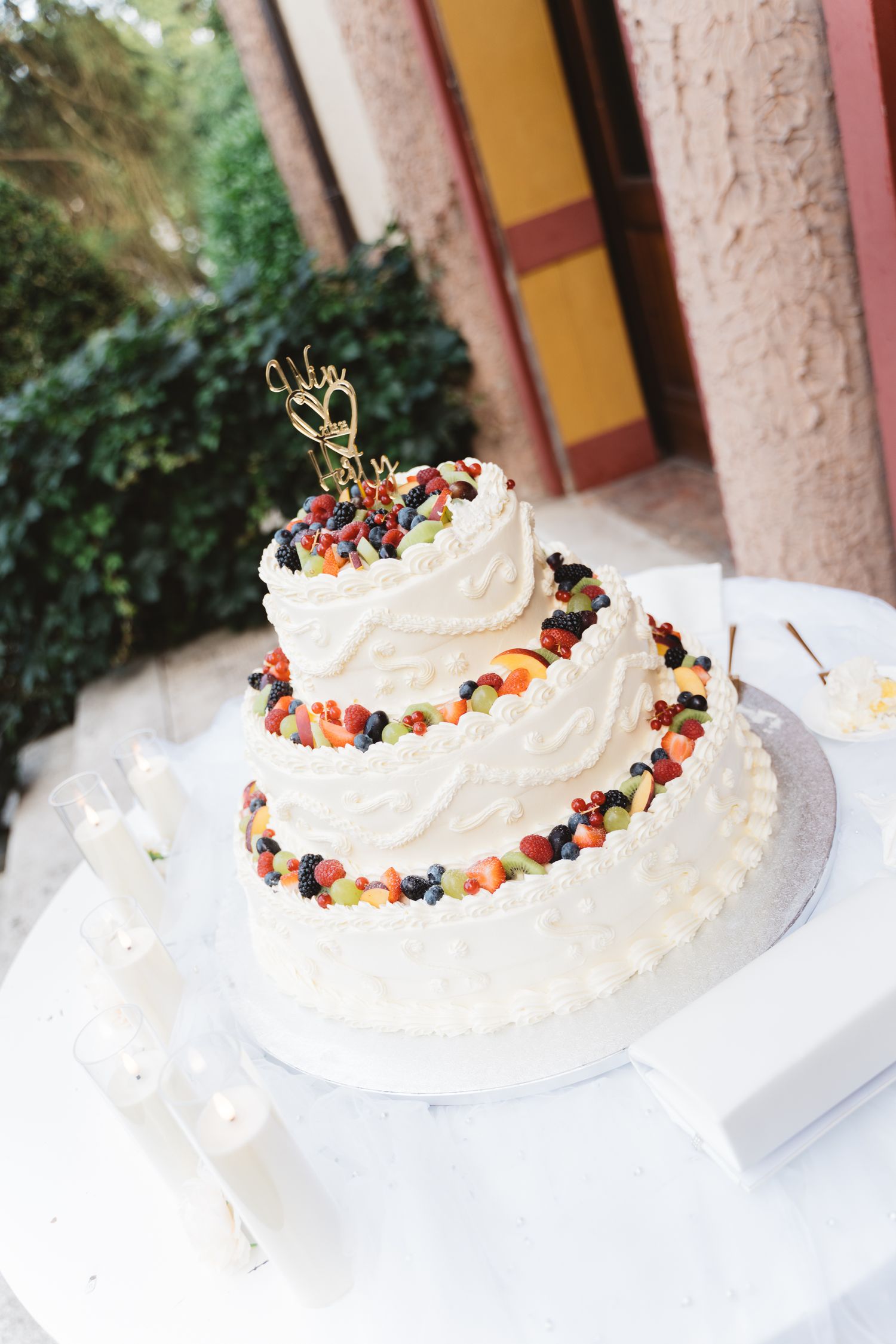 White wedding cake decorated with fresh berries and gold accents on display.
