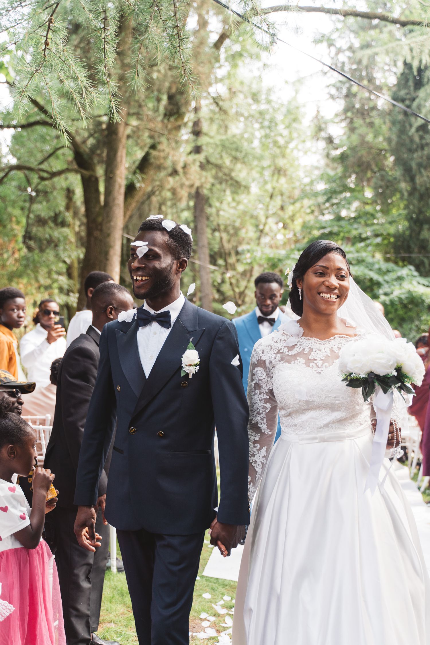 A newlywed couple smiles joyfully while walking through a wooded outdoor venue.