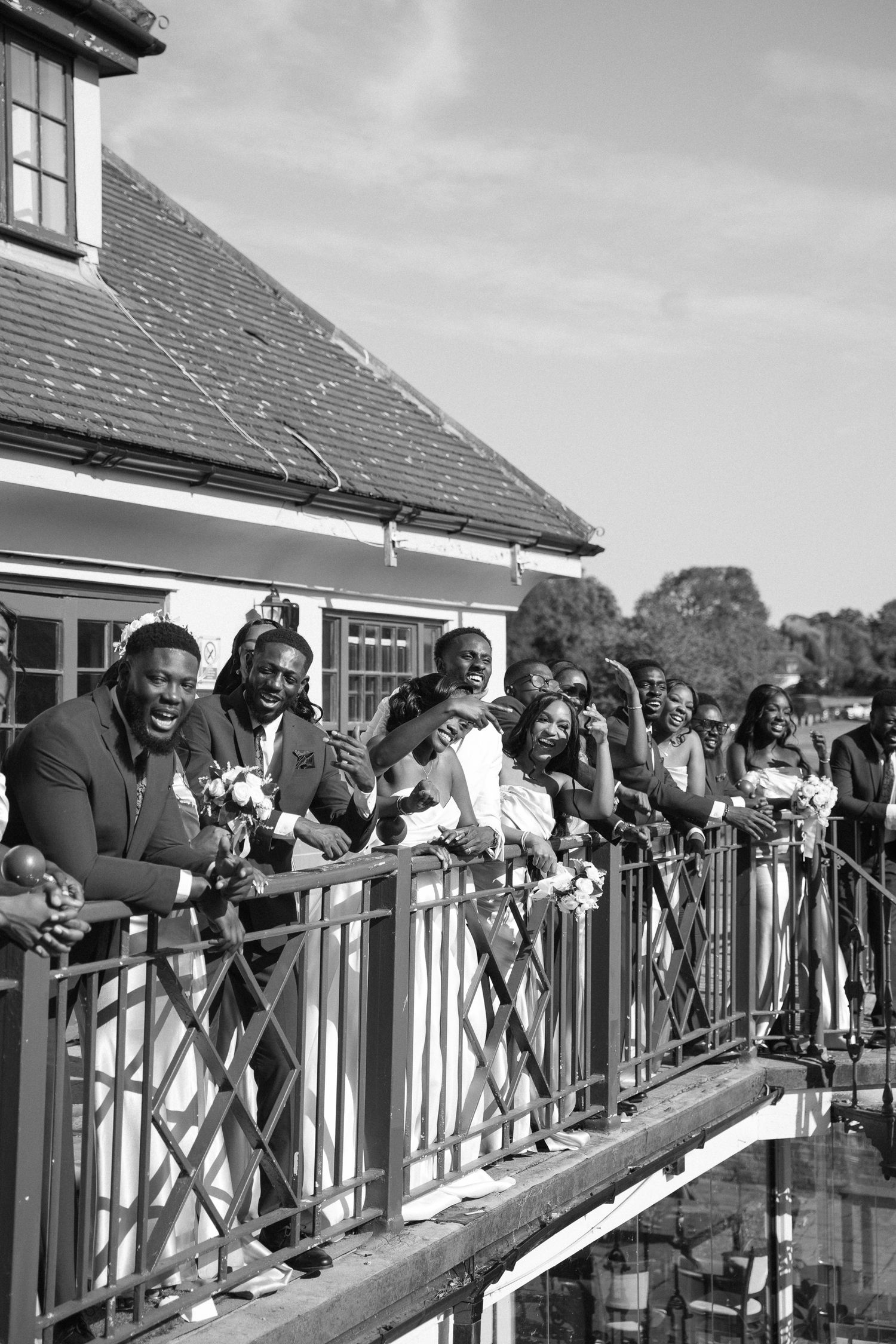 Wedding guests lean over a white railing to watch festivities below.