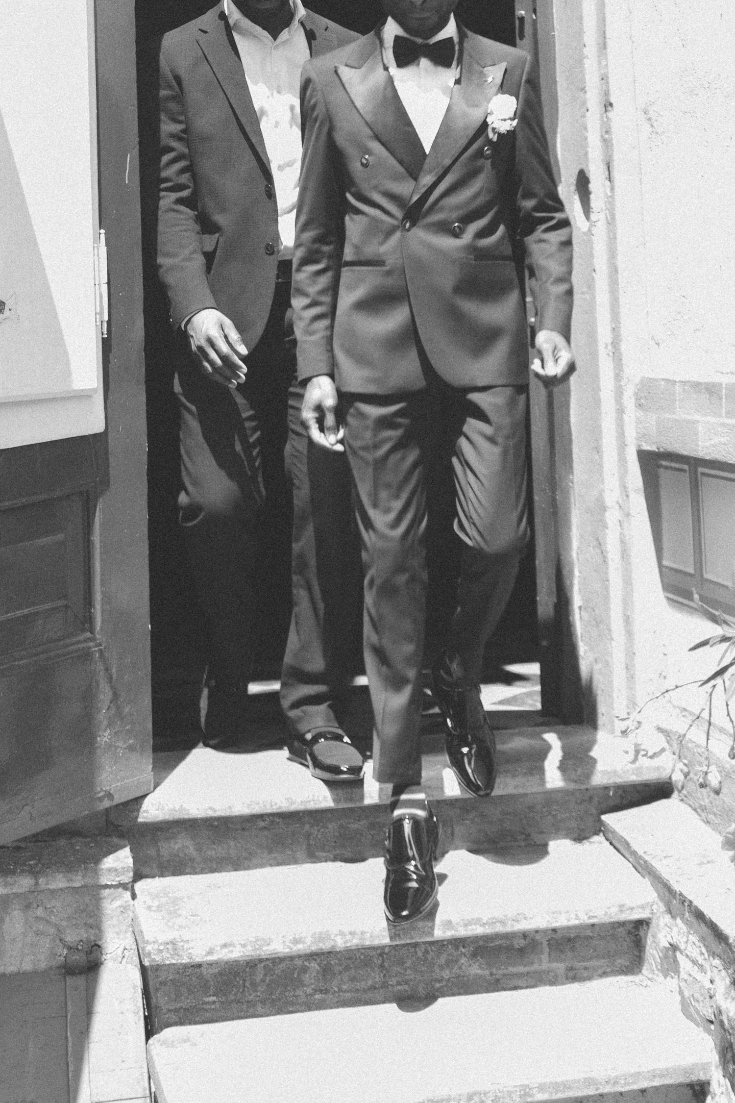 Men in formal suits walking down white church steps in black and white photo.