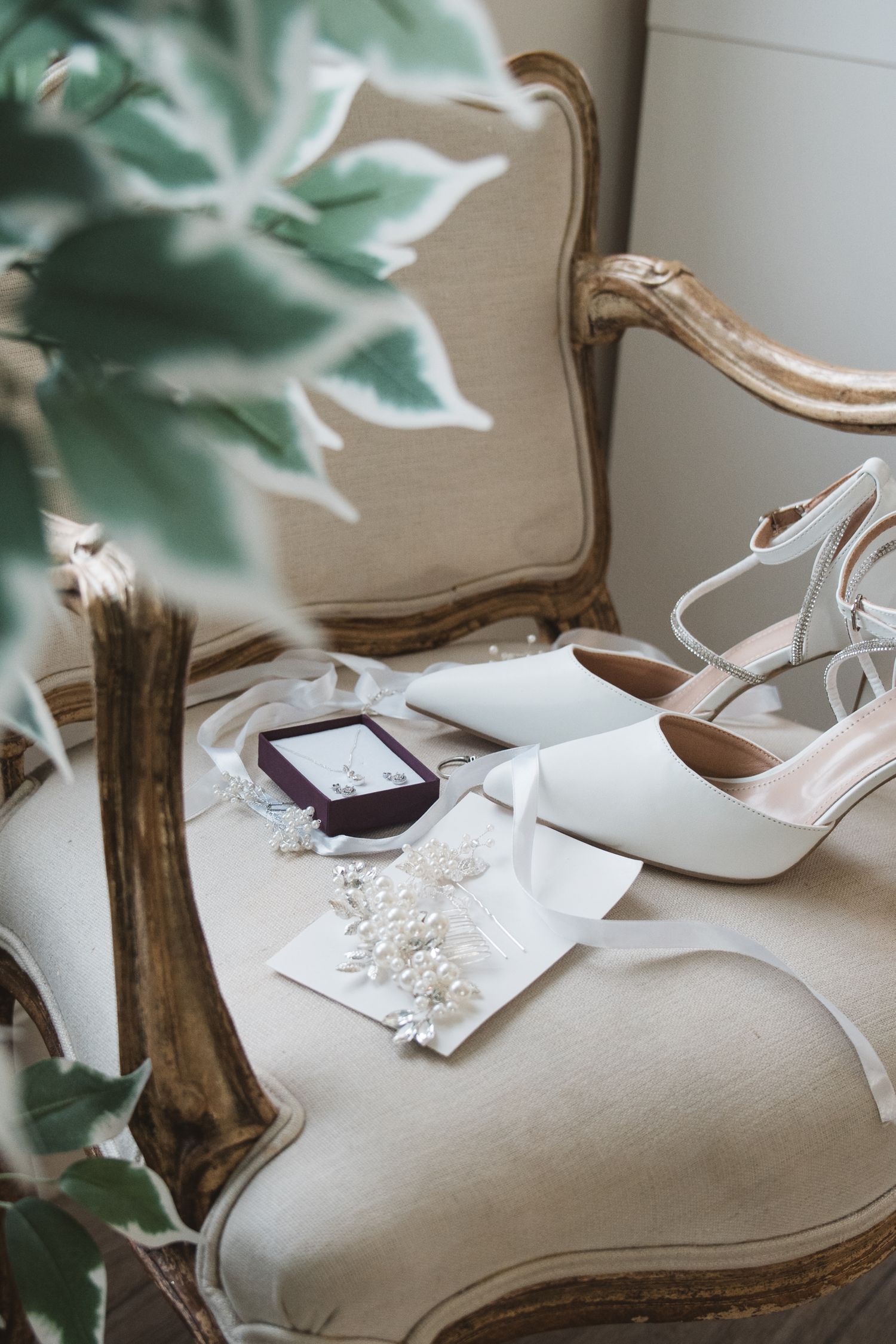 Elegant white bridal shoes and accessories arranged on vintage chair.