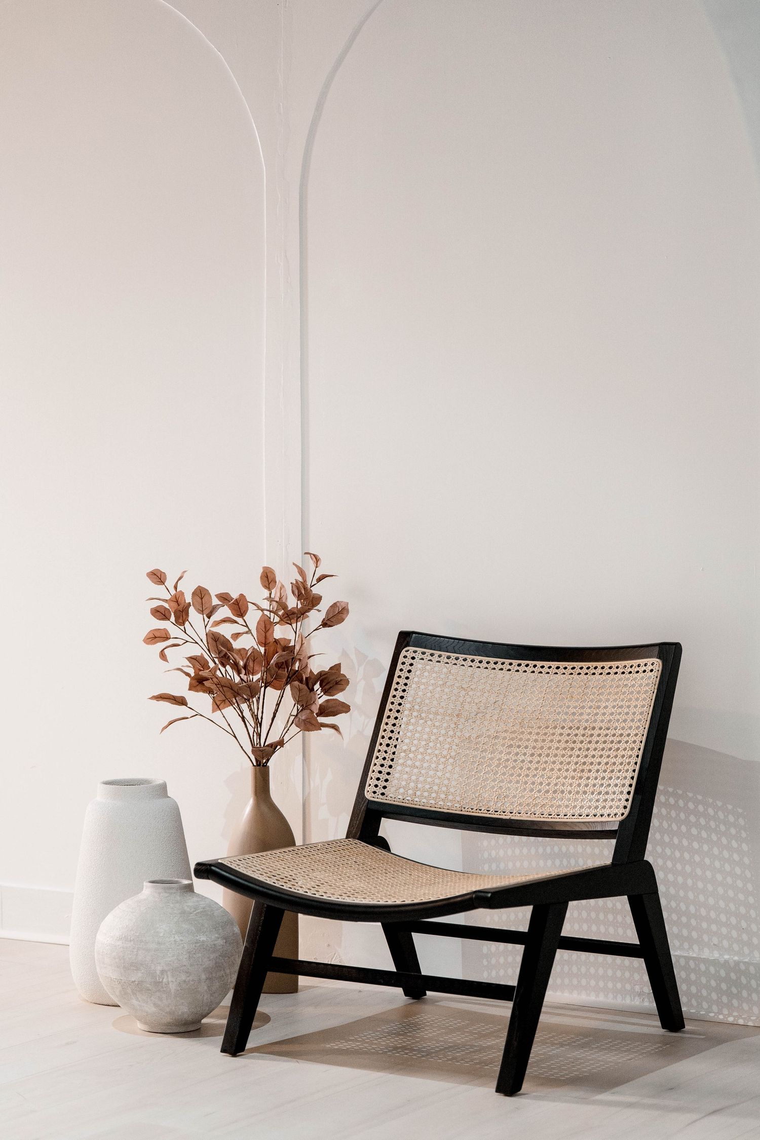 Low-profile rattan lounge chair with black frame styled with ceramic vases and dried flowers.