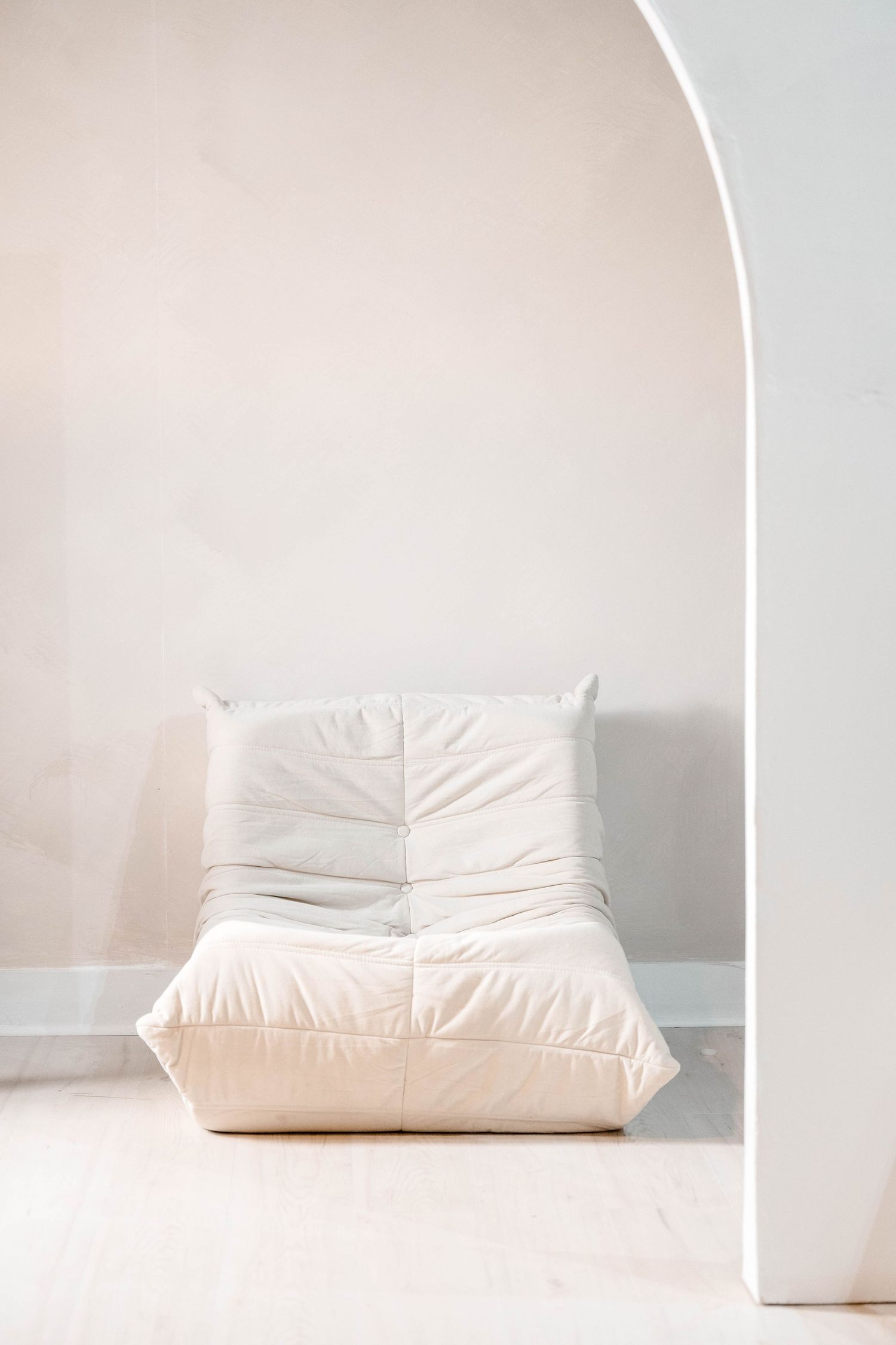 White cushioned floor chair against neutral wall in minimalist setting.