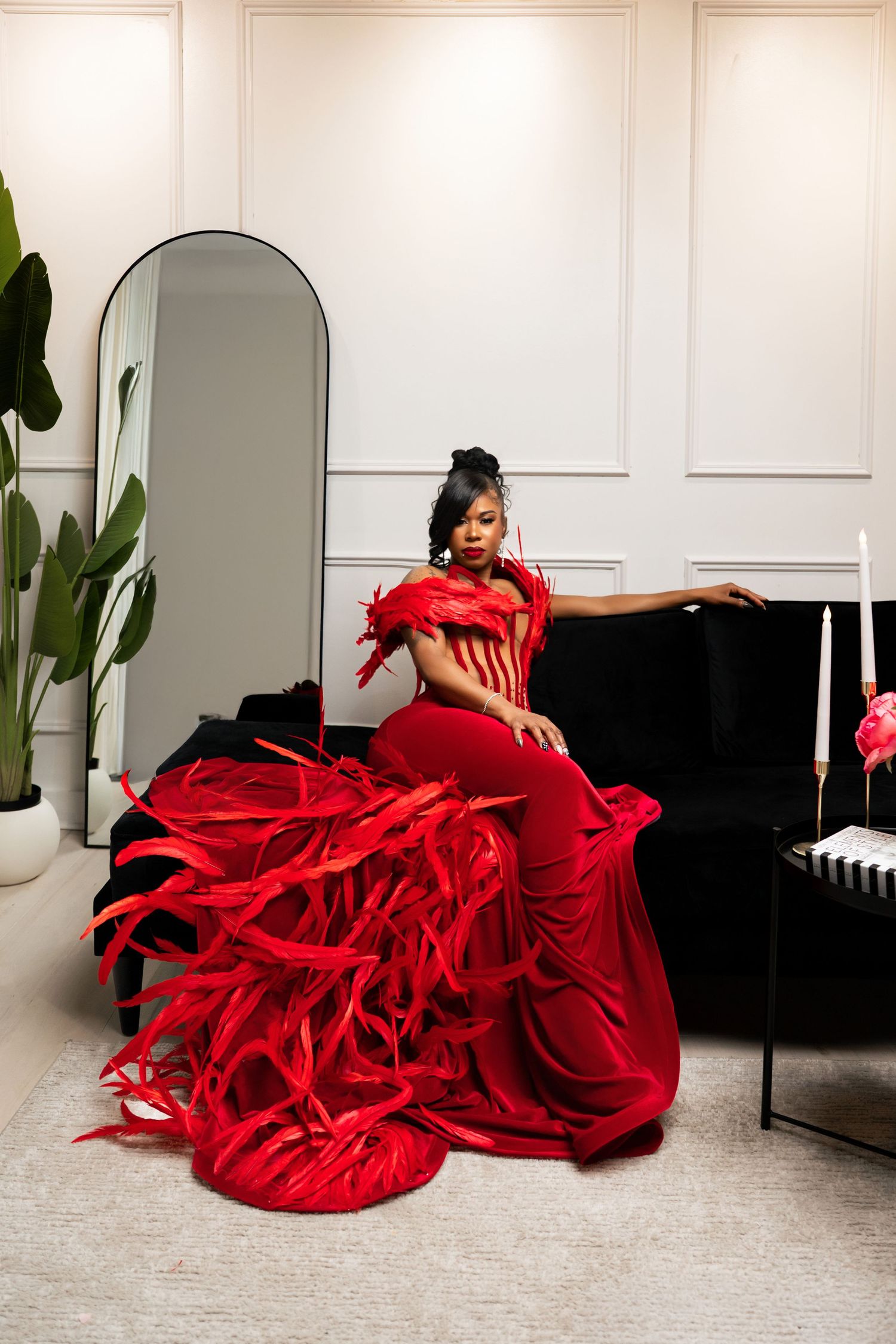 Woman in dramatic red feathered gown poses elegantly beside a black piano in a modern white interior.