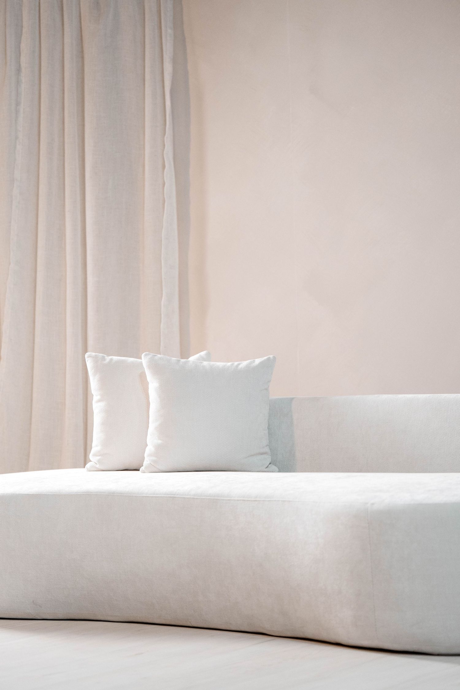 White curved sofa with throw pillows against a light neutral backdrop with soft drapery.