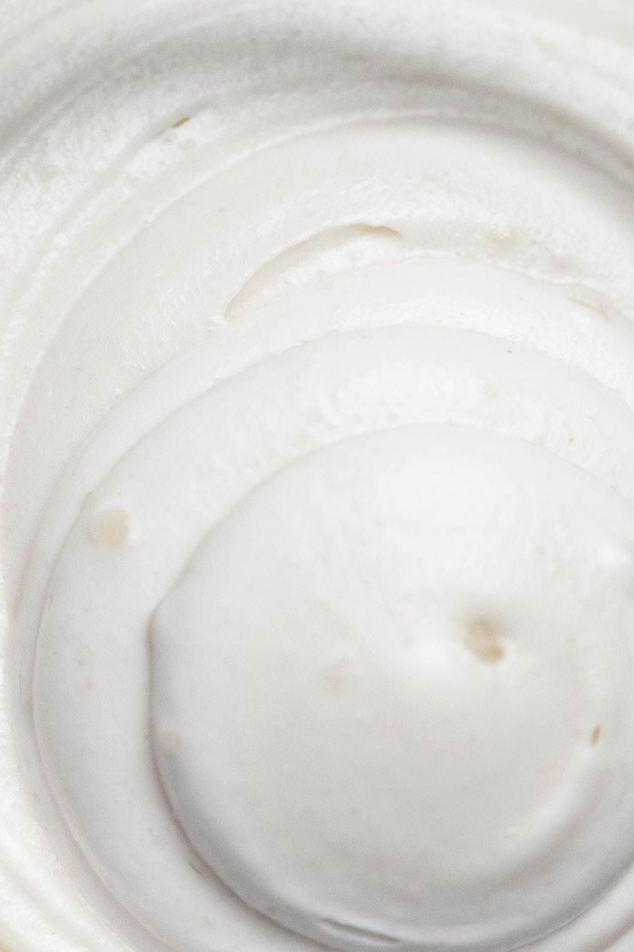 Close-up swirl of creamy white whipped cream or moisturizer with smooth texture.